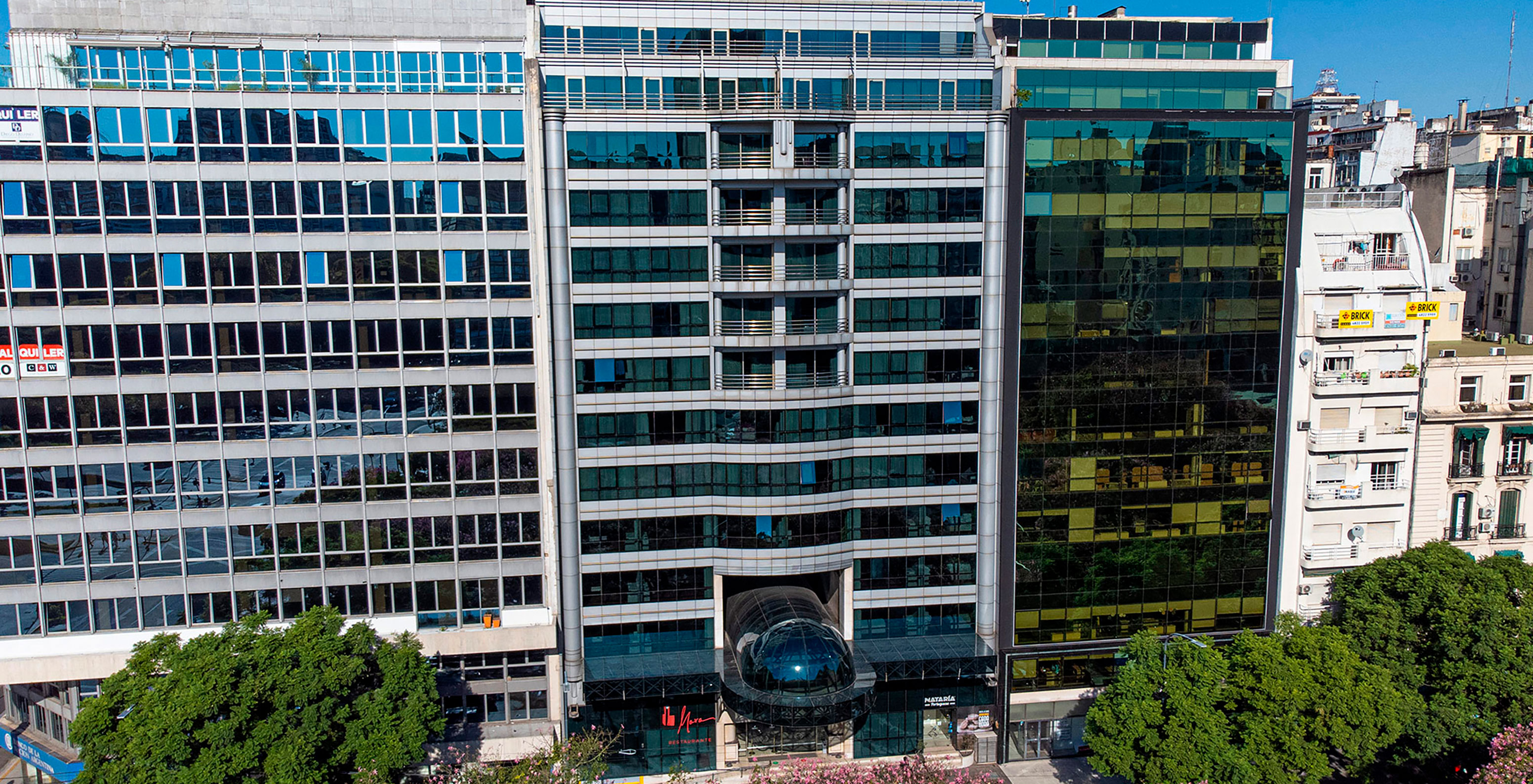 Außenansicht des Pestana Buenos Aires, ein modernes Gebäude mit spiegelverglasten Fenstern und blühenden Bäumen davor