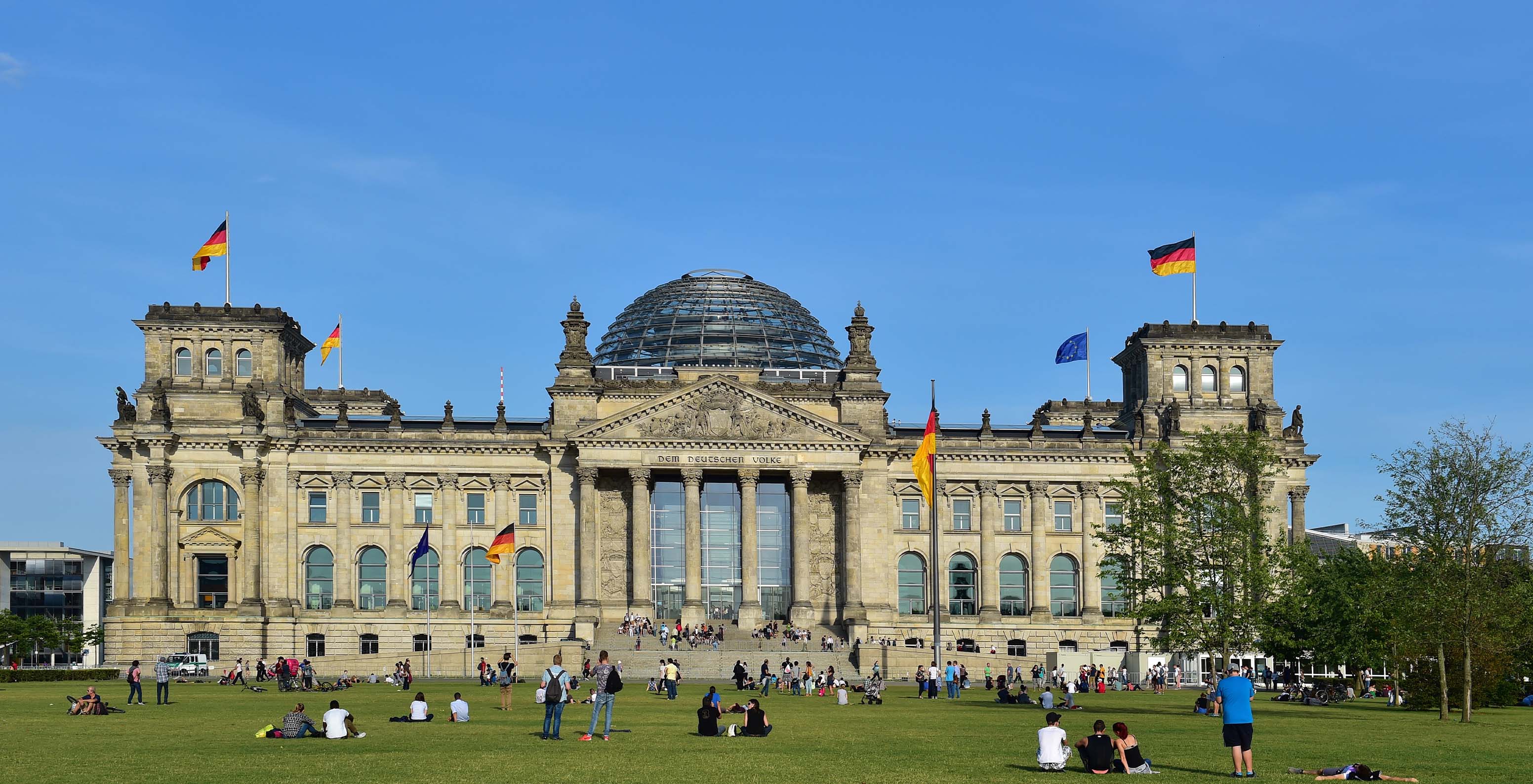 Blick auf den Reichstag, Sitz des Deutschen Parlaments in Berlin, mit Menschen im Garten, die Fotos machen und spazieren