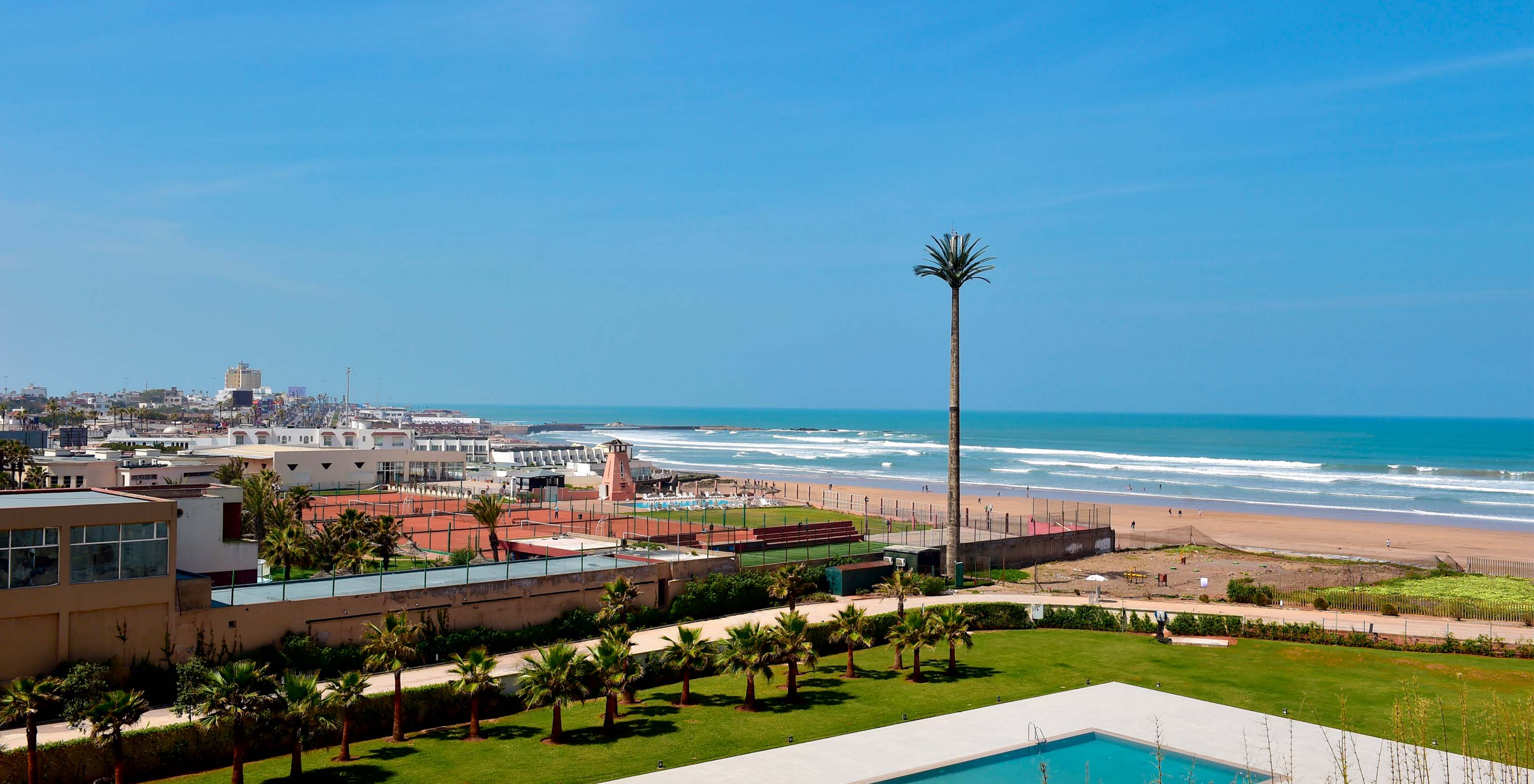 Blick von außen auf das Hotel, mit der Stadt, dem weißen Sandstrand und dem Meer im Hintergrund