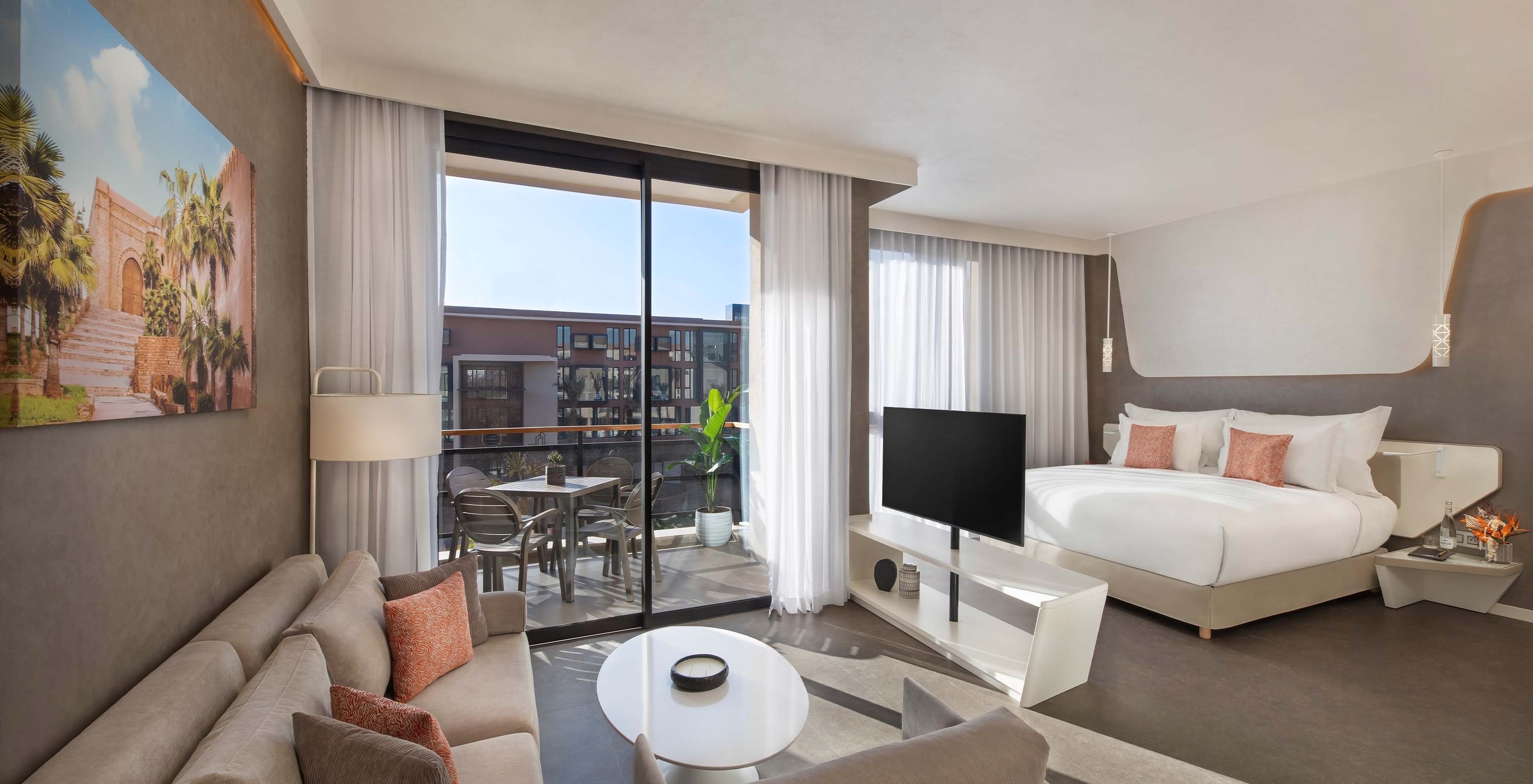 Die CR7 Junior Suite Avenue im Pestana CR7 Marrakeck hat einen Wohnbereich mit Sofas und Fernseher und einen Balkon mit Tisch