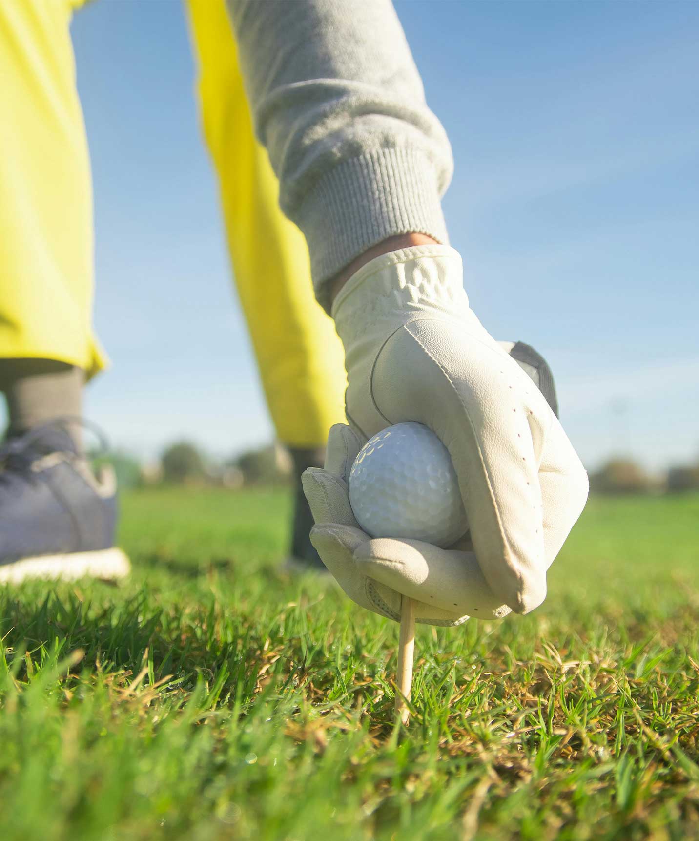 Person beugt sich zu dem Golfball auf dem Platz und bereitet den nächsten Schlag vor