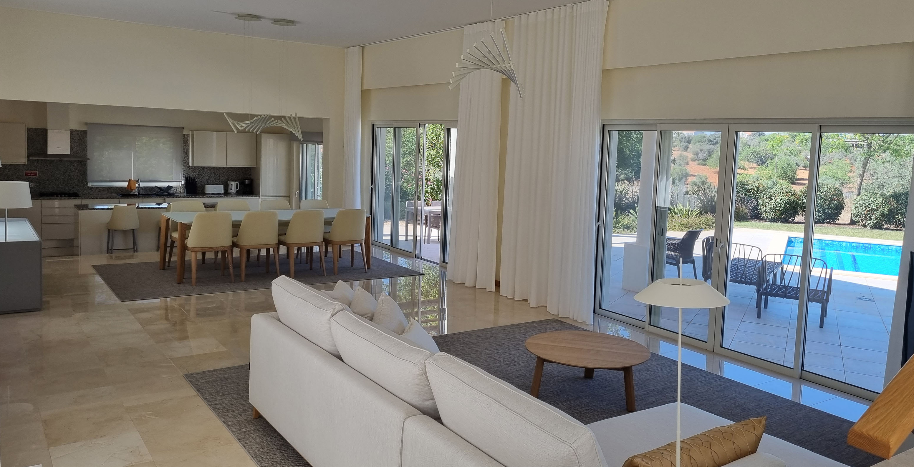 Die V5-Villa im Pestana Carvoeiro Golf hat ein Wohnzimmer mit Sofa, Tisch, offener Küche und Fenstern nach außen