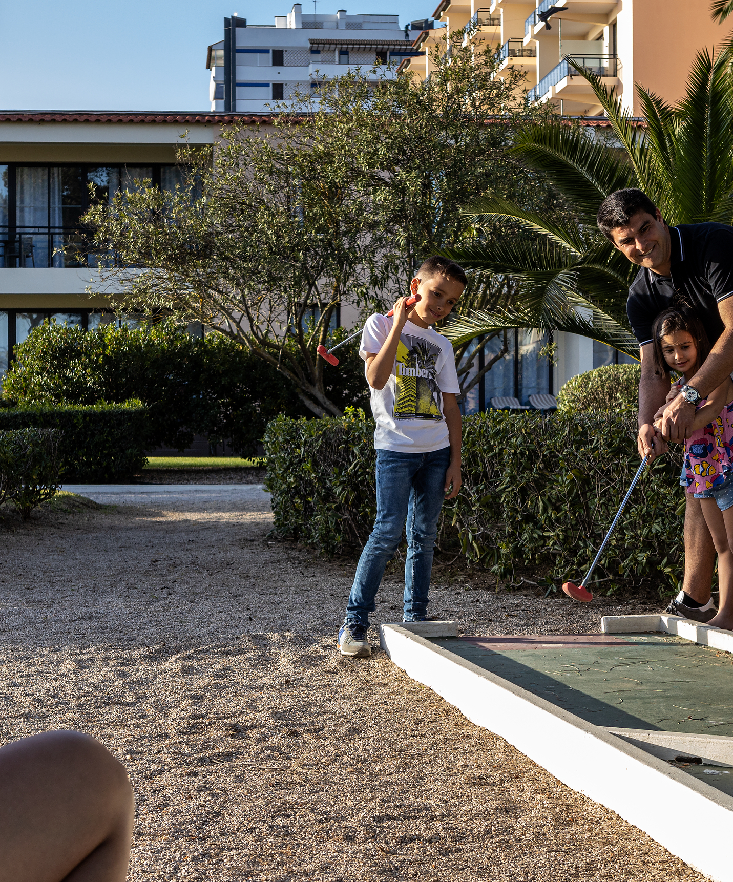 Minigolfloch mit grünem Rasenboden, einem roten und einem grünen Schläger, zwei orange und einem weißen Golfball