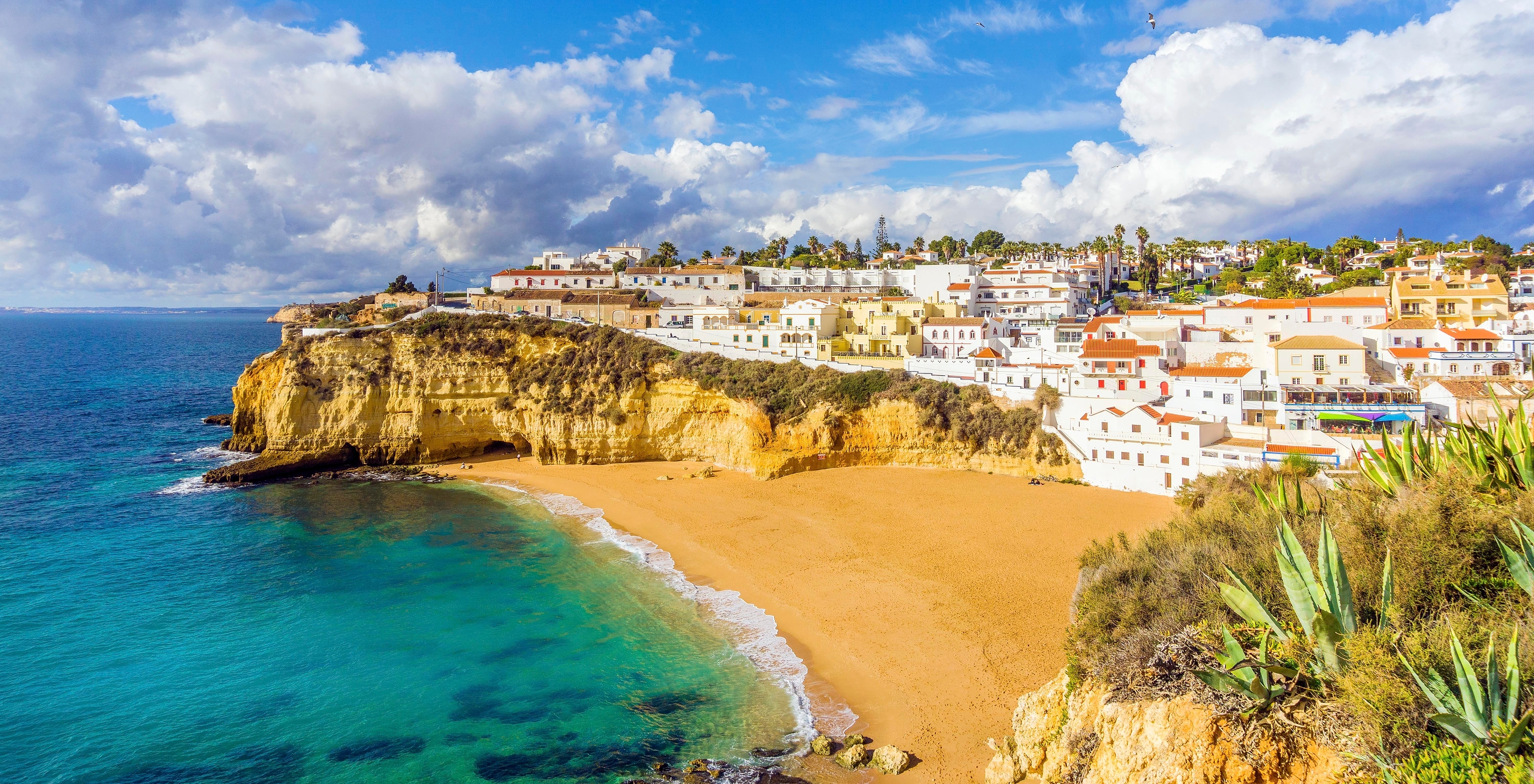 Strand von Carvoeiro, mit blauem Wasser, typischen Algarve-Felsen und dem Dorf Carvoeiro im Hintergrund