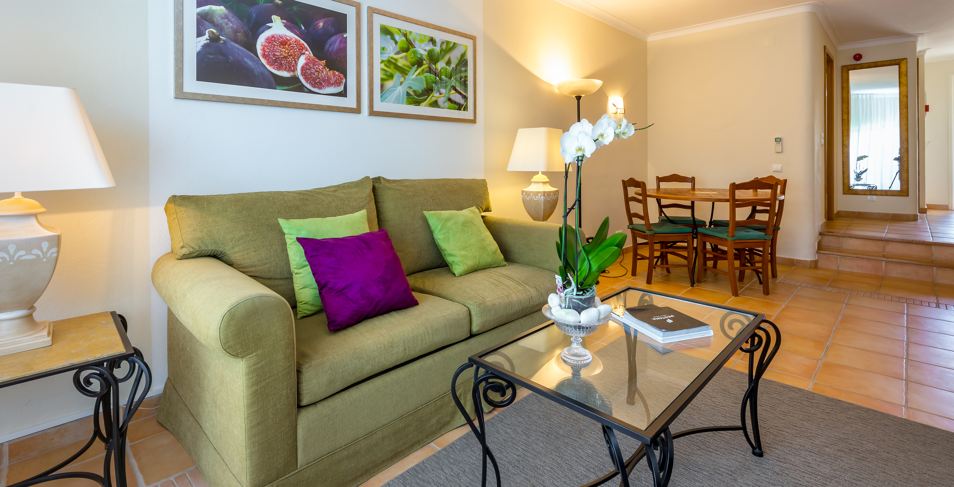 Das T2 Standard Appartement im Pestana Palm Gardens hat ein Wohnzimmer mit Sofa, Kissen, einem runden Tisch und Bildern