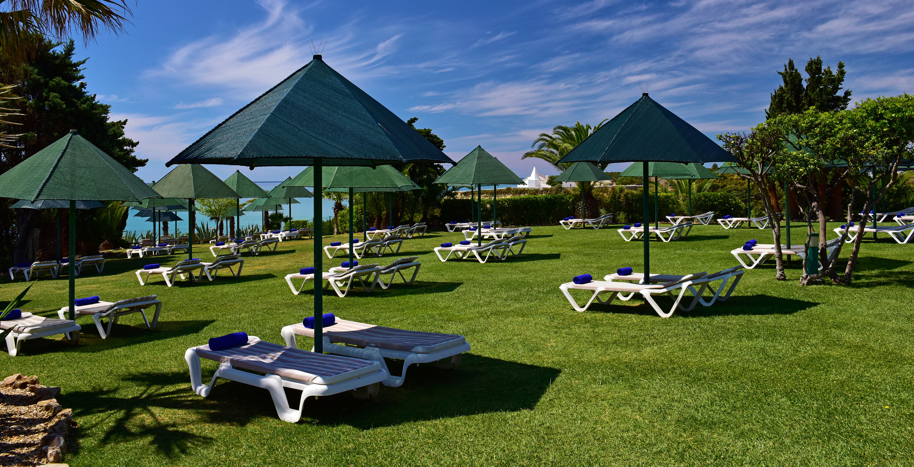 Außenansicht des Pestana Viking mit Liegen und Sonnenschirmen auf dem Rasen und blauem Meer im Hintergrund