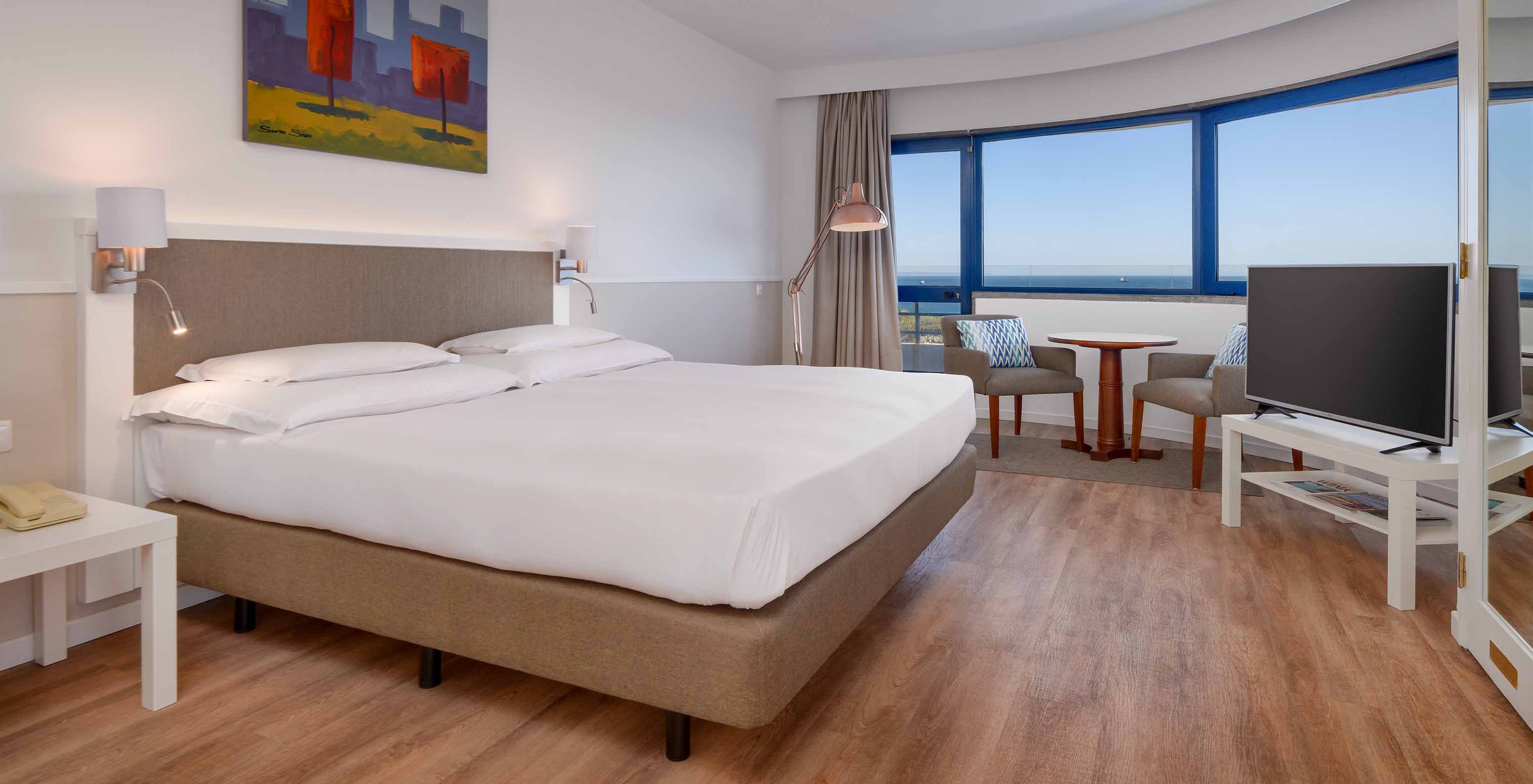 Die Deluxe Suite mit Meerblick im Pestana Cascais hat ein Doppelbett, TV und ein Bild an der Wand