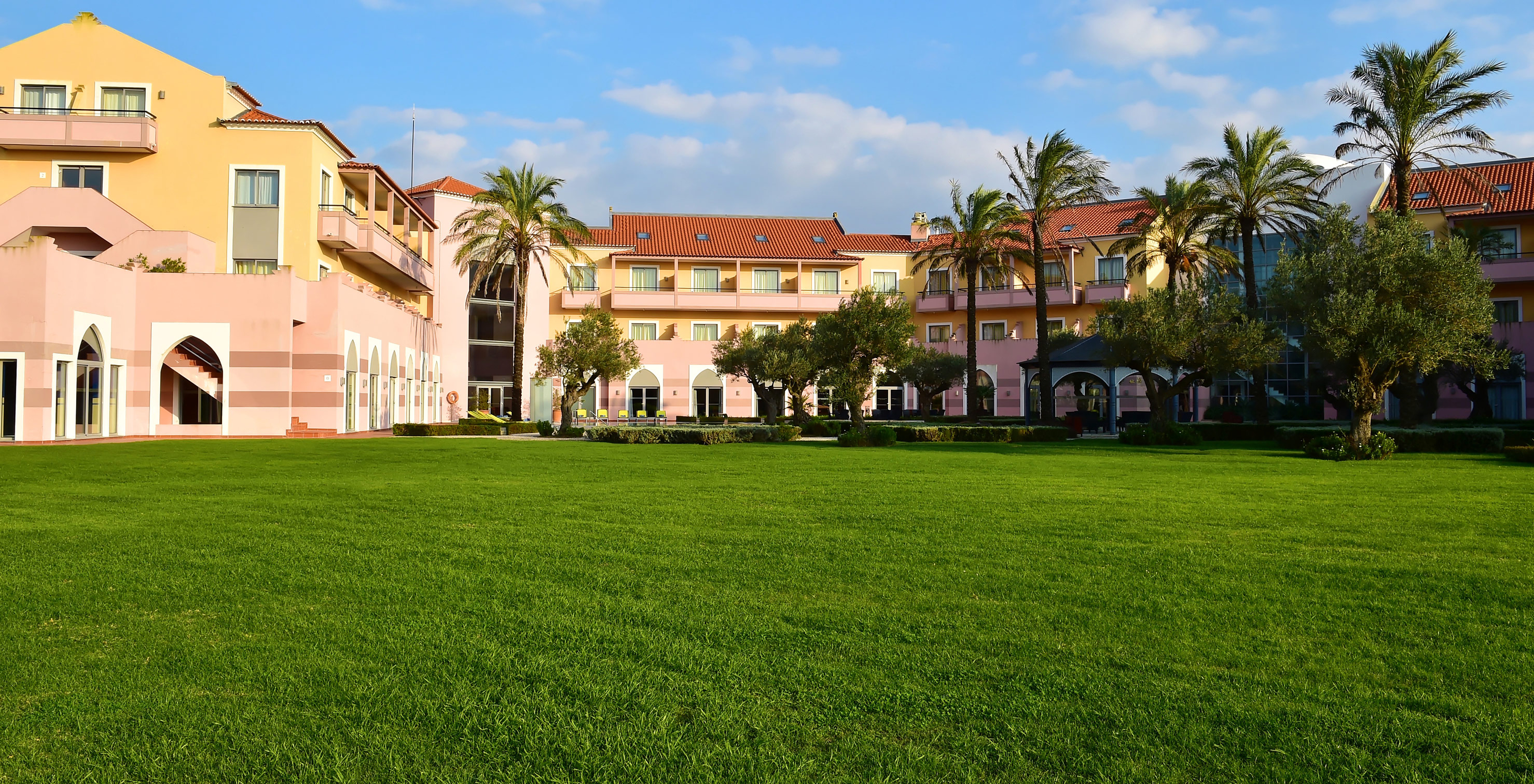 Gebäude des Pestana Sintra Golf, umgeben von grünem Vegetation, Palmen und Bäumen an einem sonnigen Tag mit blauem Himmel