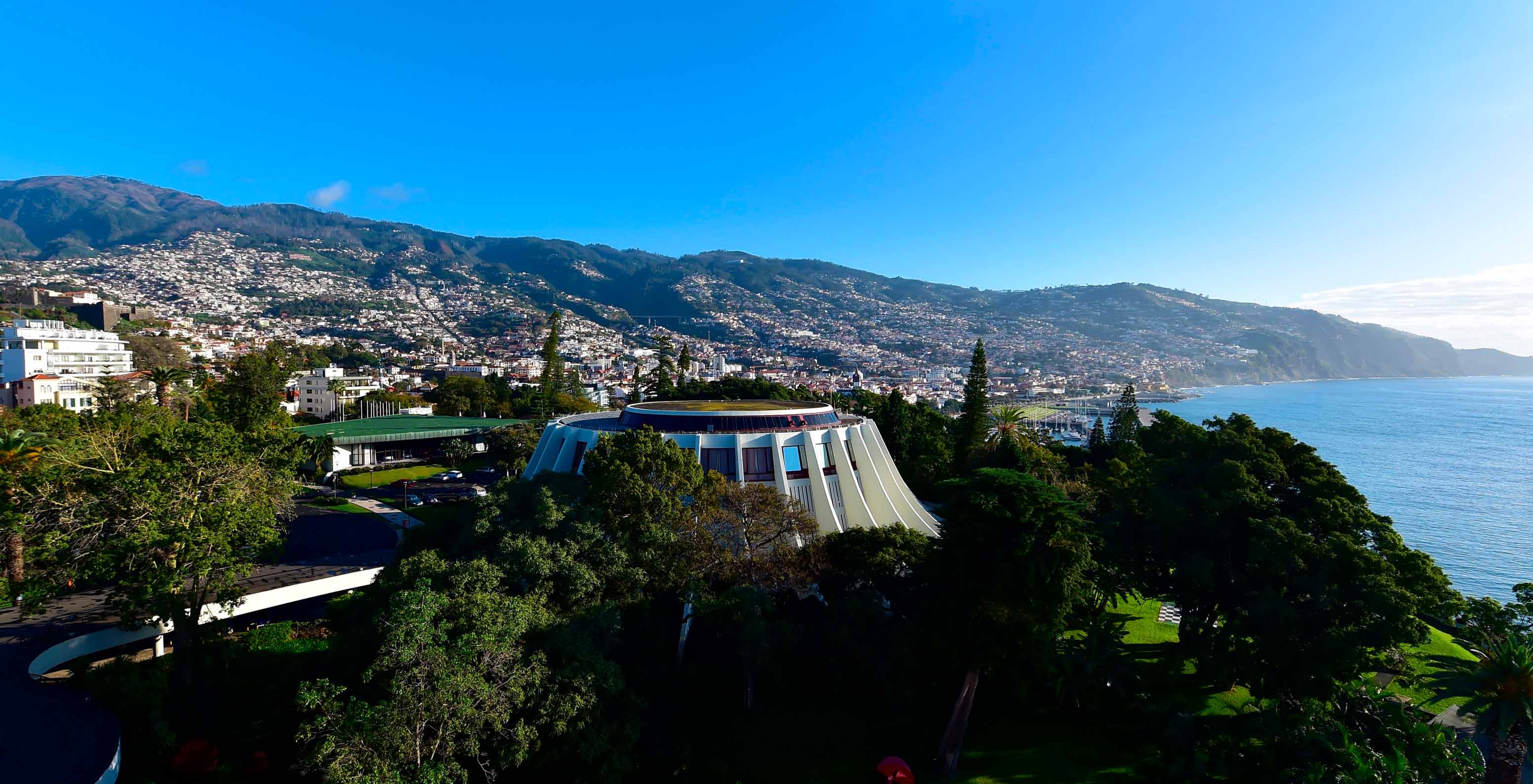 Außenansicht des Casinos von Madeira, nahe dem Pestana Casino Park, umgeben von Vegetation, Stadt und Meer im Hintergrund