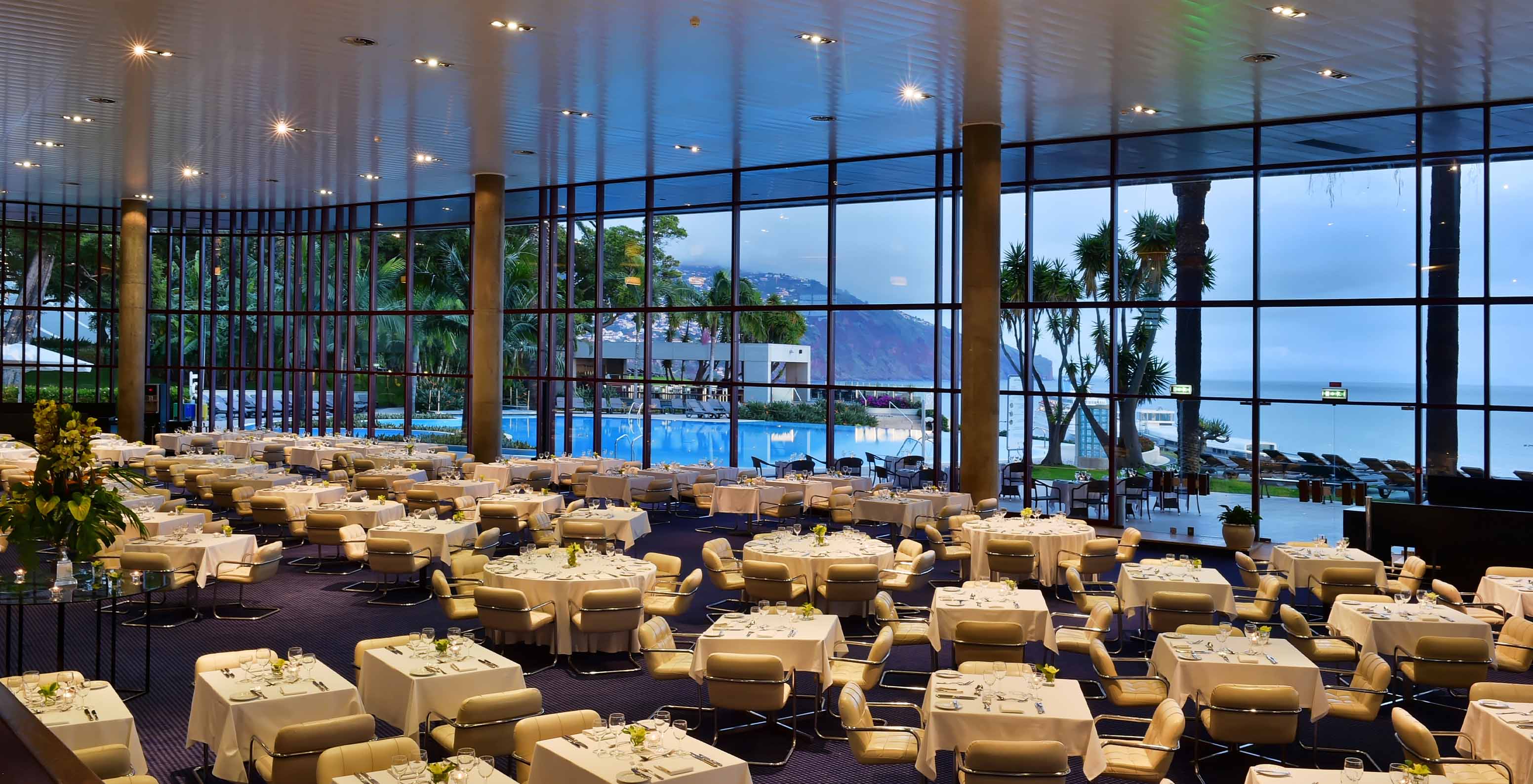 Das Restaurant Panorâmico, im Hotel in Funchal, auf der Insel Madeira, hat mehrere Tische und gepolsterte Stühle in Beige