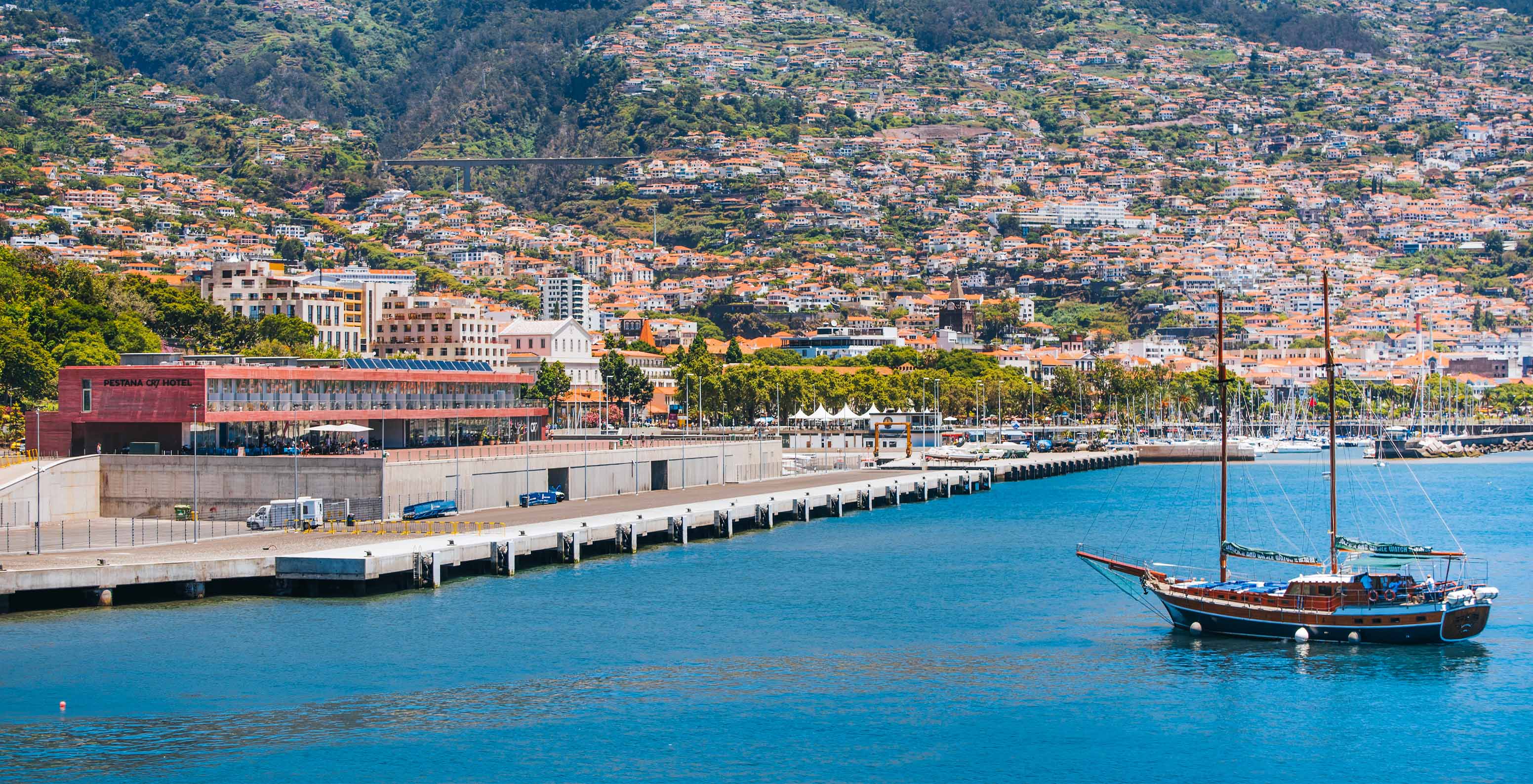 Blick auf den Hafen der Stadt Funchal, mit dem Hang der Stadt im Hintergrund und einem Boot im Meer