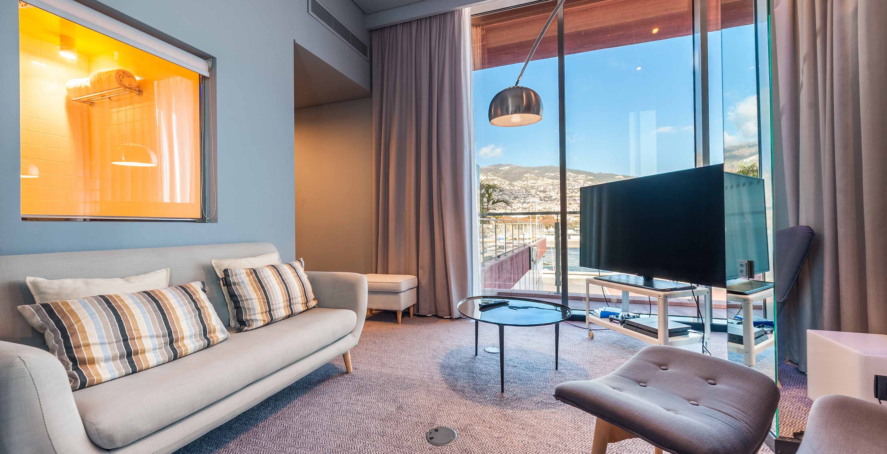 Die CR7 Suite im Pestana CR7 Funchal hat ein Wohnzimmer mit Sofa, Fernseher und Fenster mit Blick auf Funchal