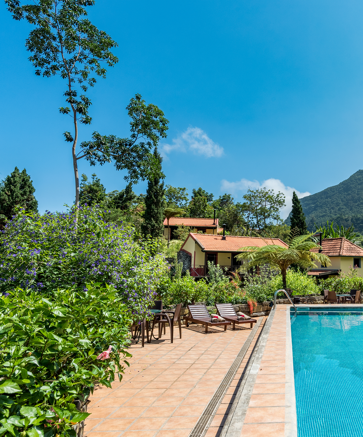 Pool des Pestana Quinta do Arco mit Liegen und Sonnenschirm, Vegetation und Villen mit Bergen im Hintergrund