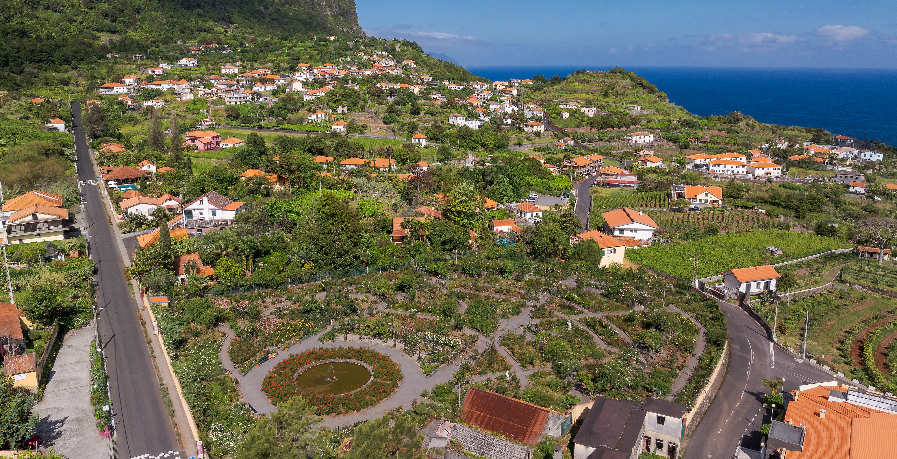 Luftaufnahme des Pestana Quinta do Arco mit Bergen, Häusern, Rosengarten und grünen Feldern mit dem Ozean im Hintergrund