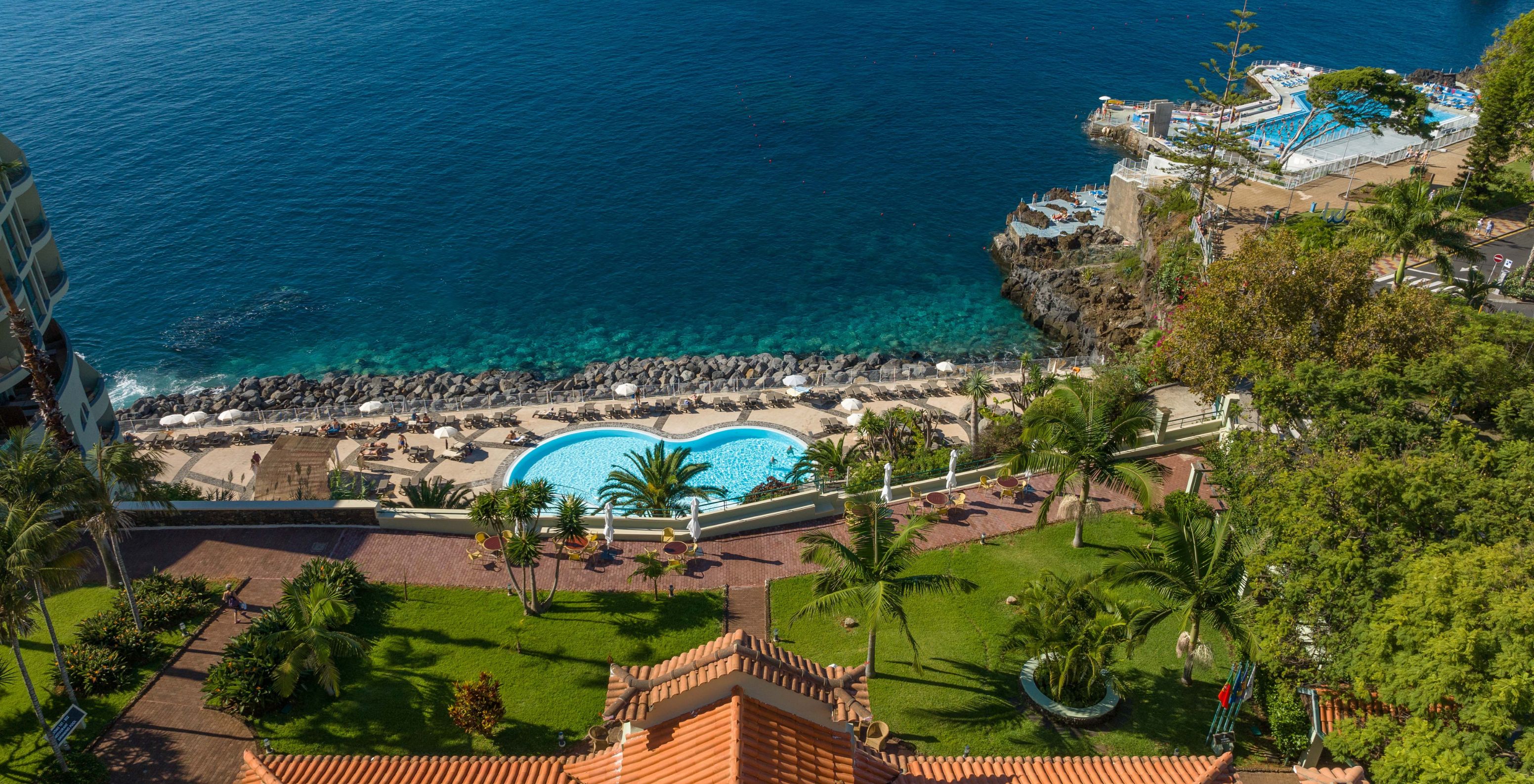 Das Pestana Vila Lido Madeira hat Gärten neben dem Hotelgebäude, mit Palmen, Gras und Sträuchern