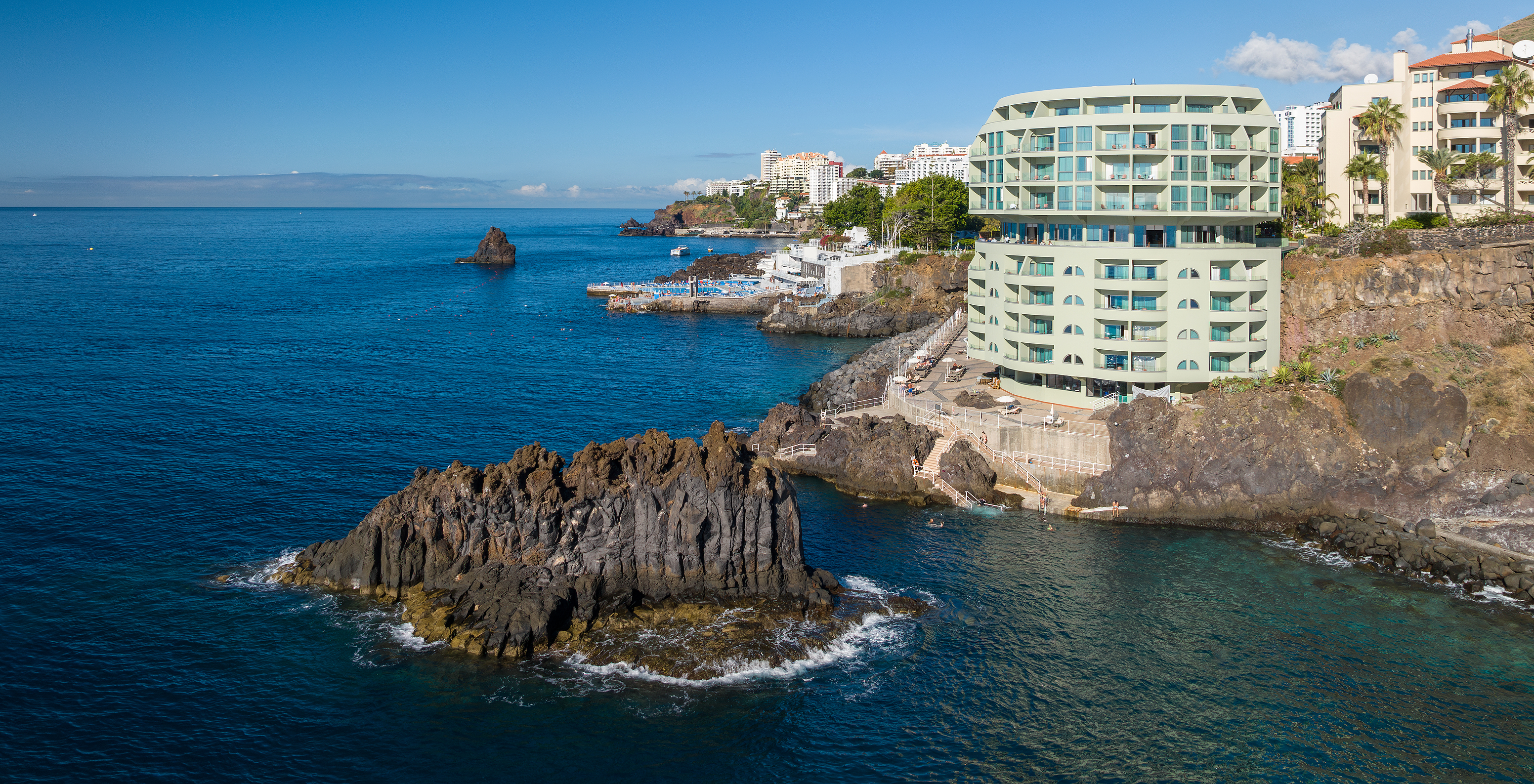 Blick auf das Pestana Vila Lido Madeira, ein grünes Gebäude mit direktem Zugang zum Meer und mehreren Balkonen