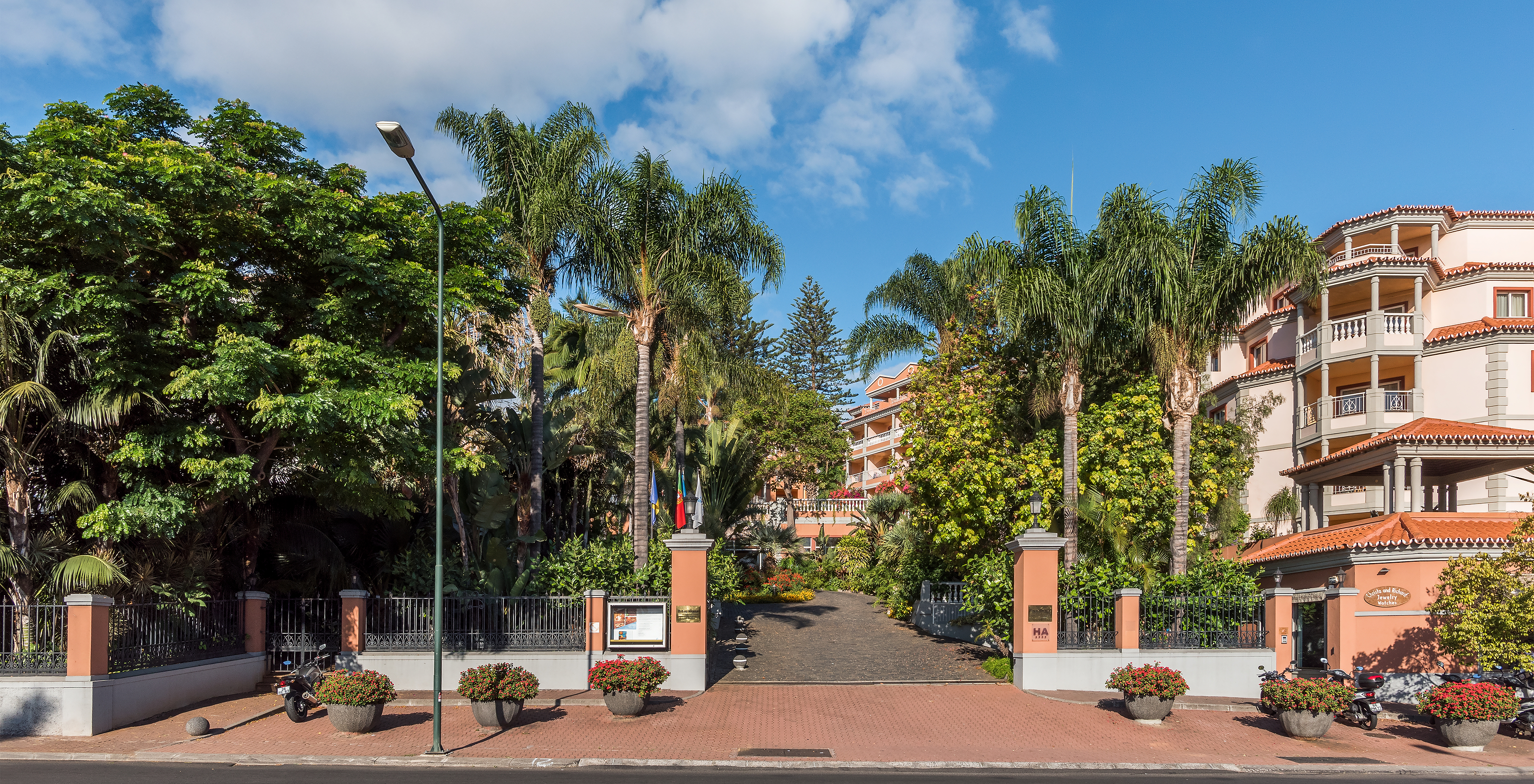 Eingang des Pestana Village, einem romantischen Hotel in Funchal, Madeira, mit mehreren Palmen und orangefarbenen Gebäuden