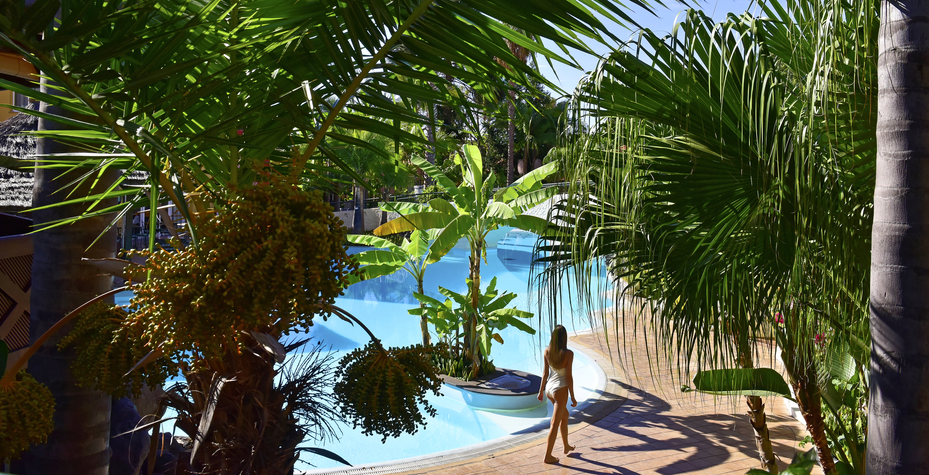 Frau, die am Pool des Pestana Village, einem romantischen Hotel in Funchal, Madeira, umgeben von Palmen spaziert