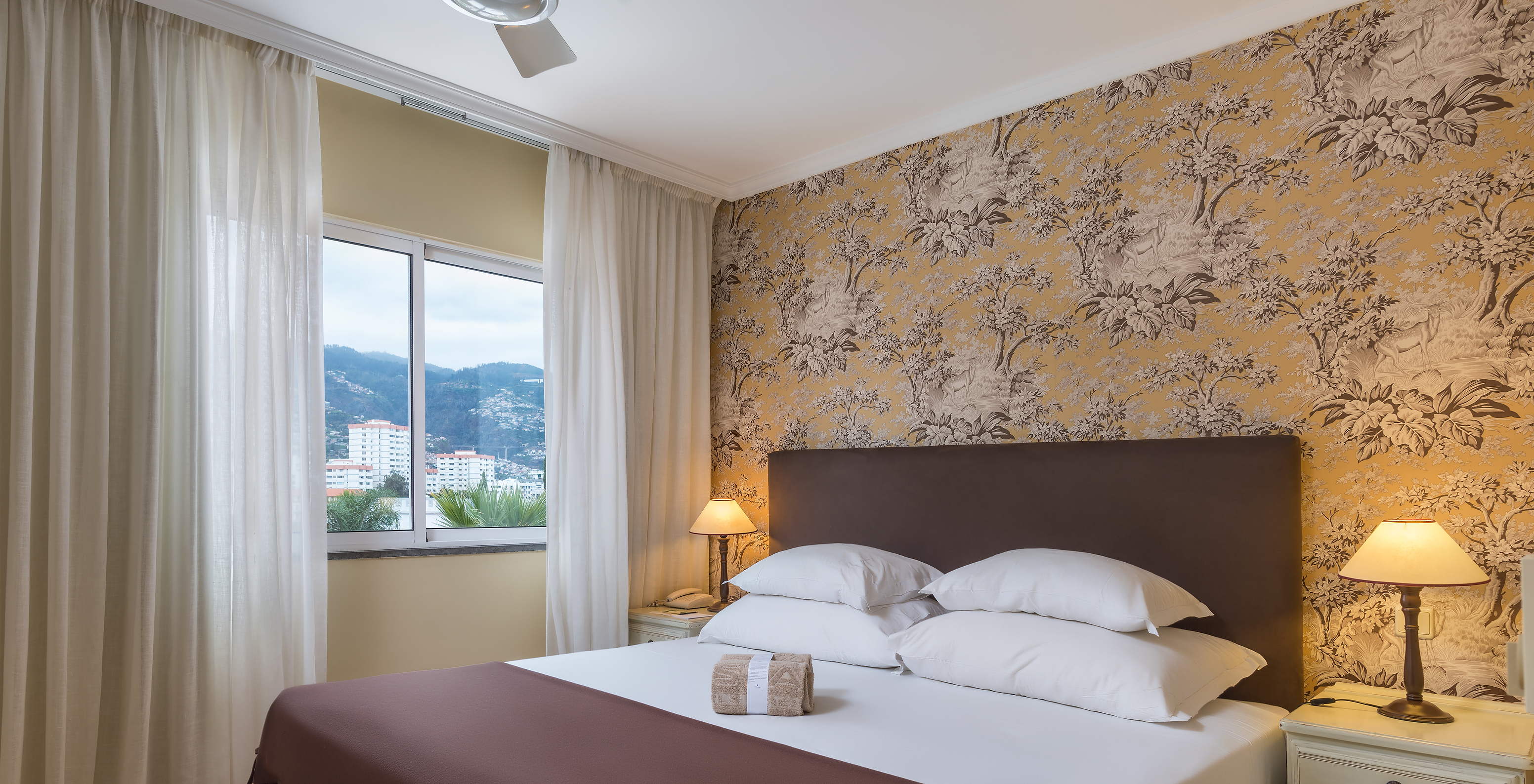 Superior Familie Pestana Village hat ein Doppelbett mit Kopfteil und braunem Überwurf, Blumentapete und Balkon