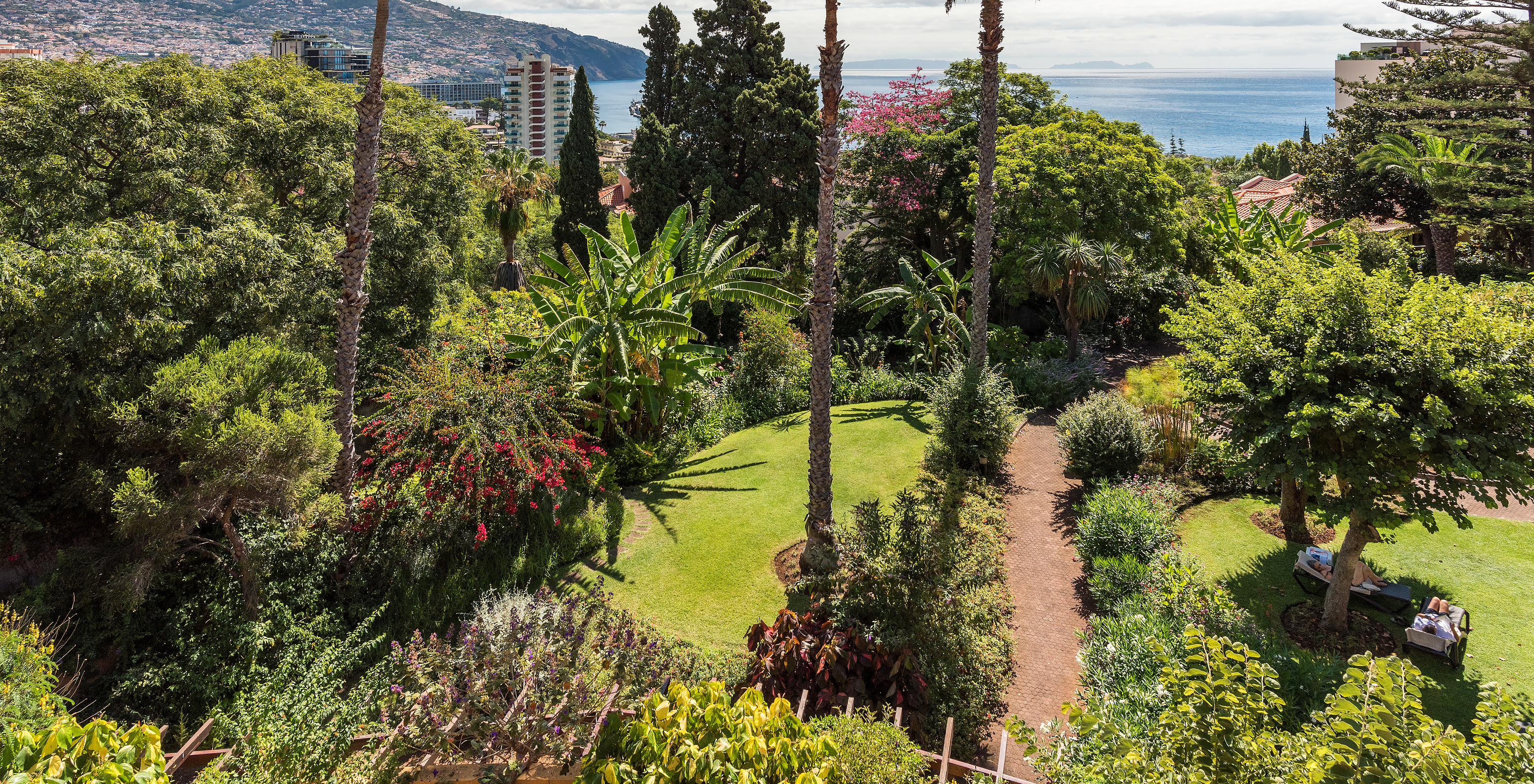 Luftaufnahme der grünen Gärten mit Blumen und Palmen im Pestana Village, einem romantischen Hotel in Funchal, Madeira