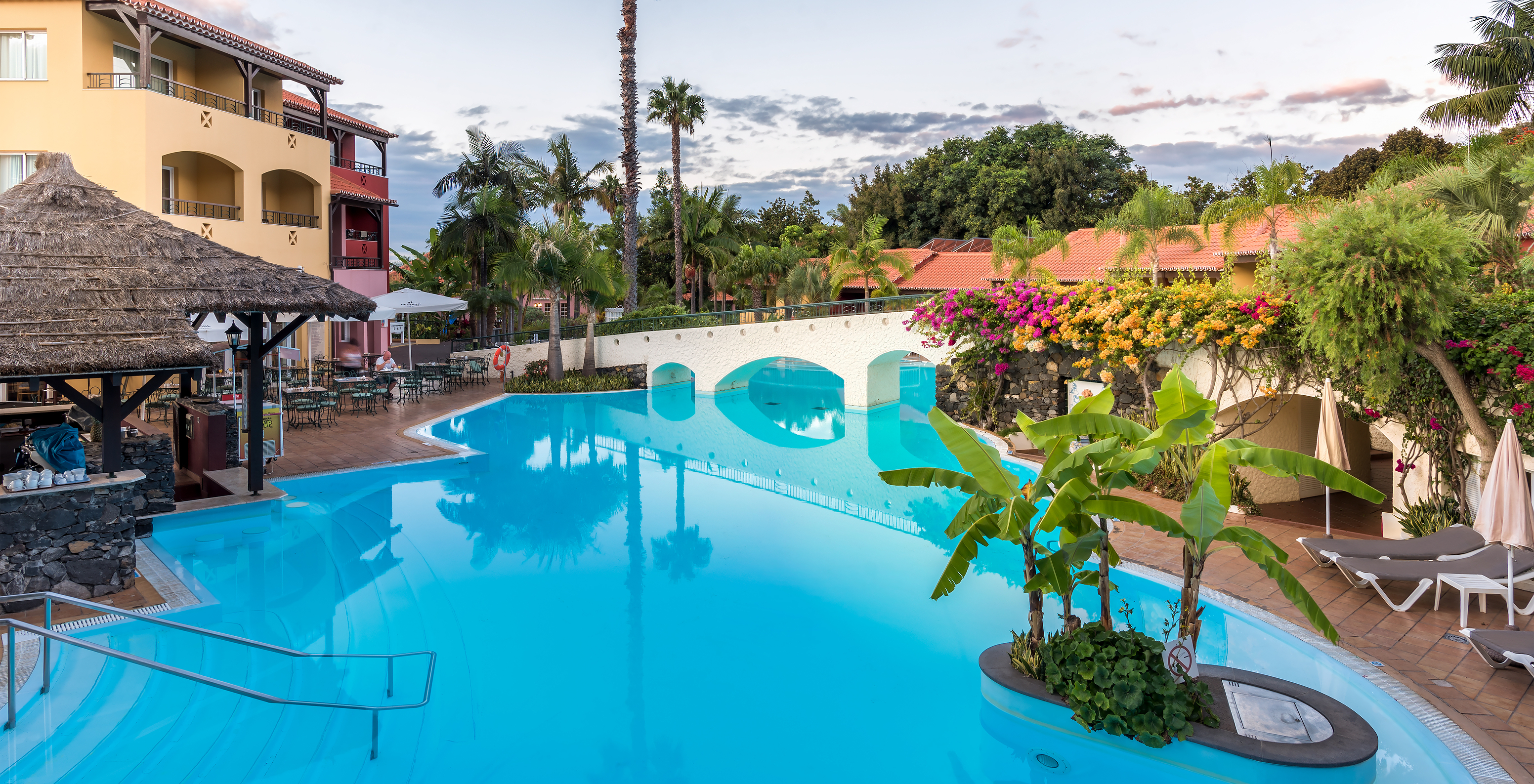 Pool des Pestana Village, einem romantischen Hotel in Funchal, Madeira, umgeben von Bäumen und Liegen