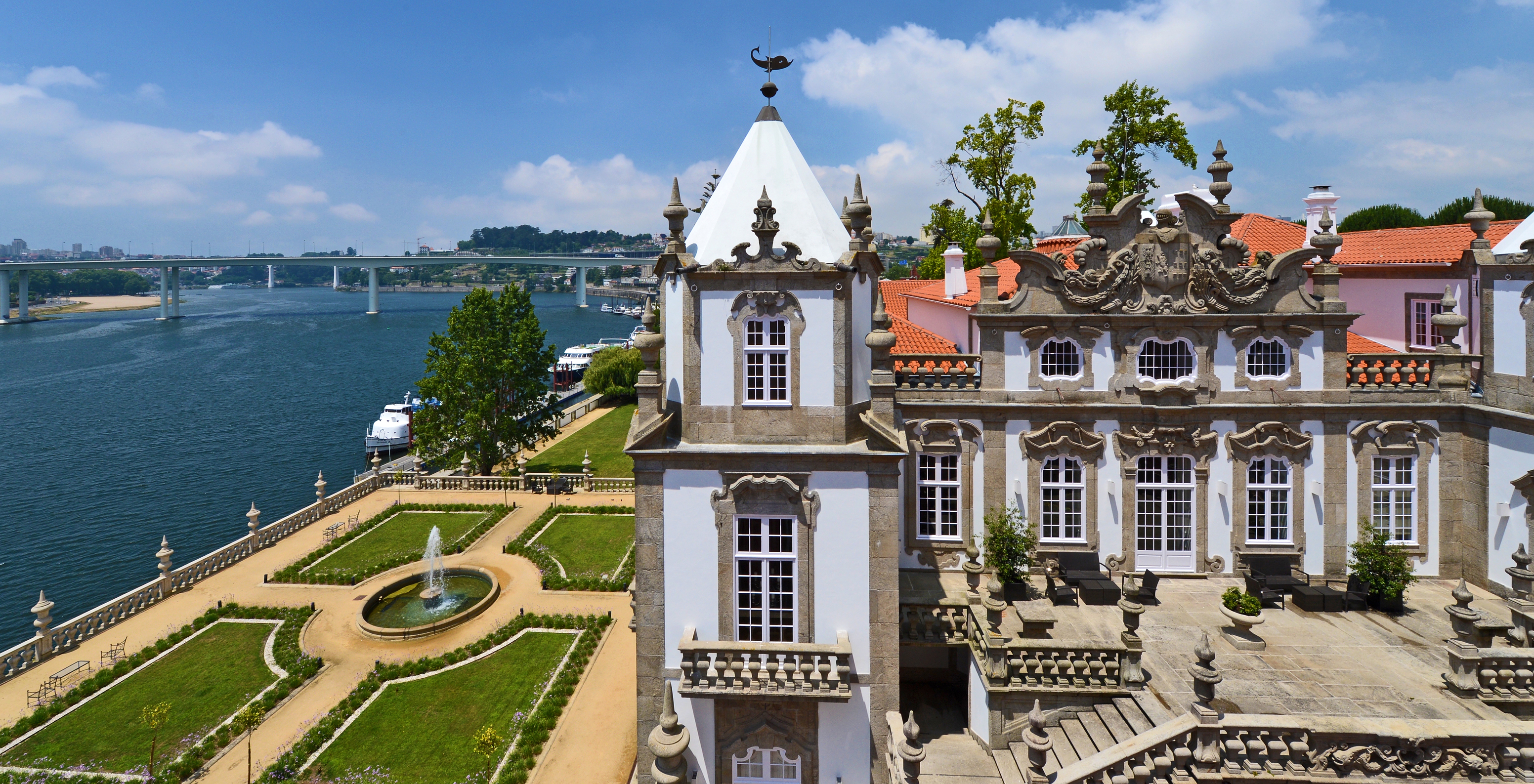 Fassade des Pestana Palácio do Freixo tagsüber, mit einem gepflegten Garten drumherum und dem Douro im Hintergrund