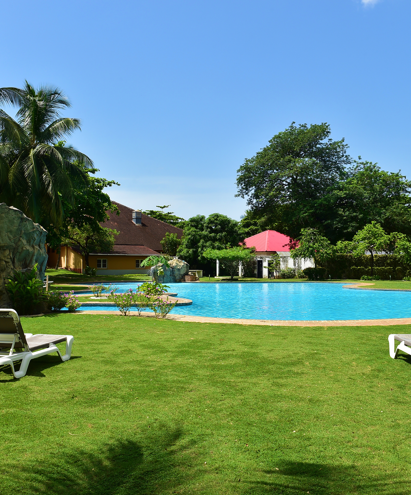 Außenpool mit Liegen im Garten mit grünem Rasen und Bäumen des Hotels mit Pool am Strand