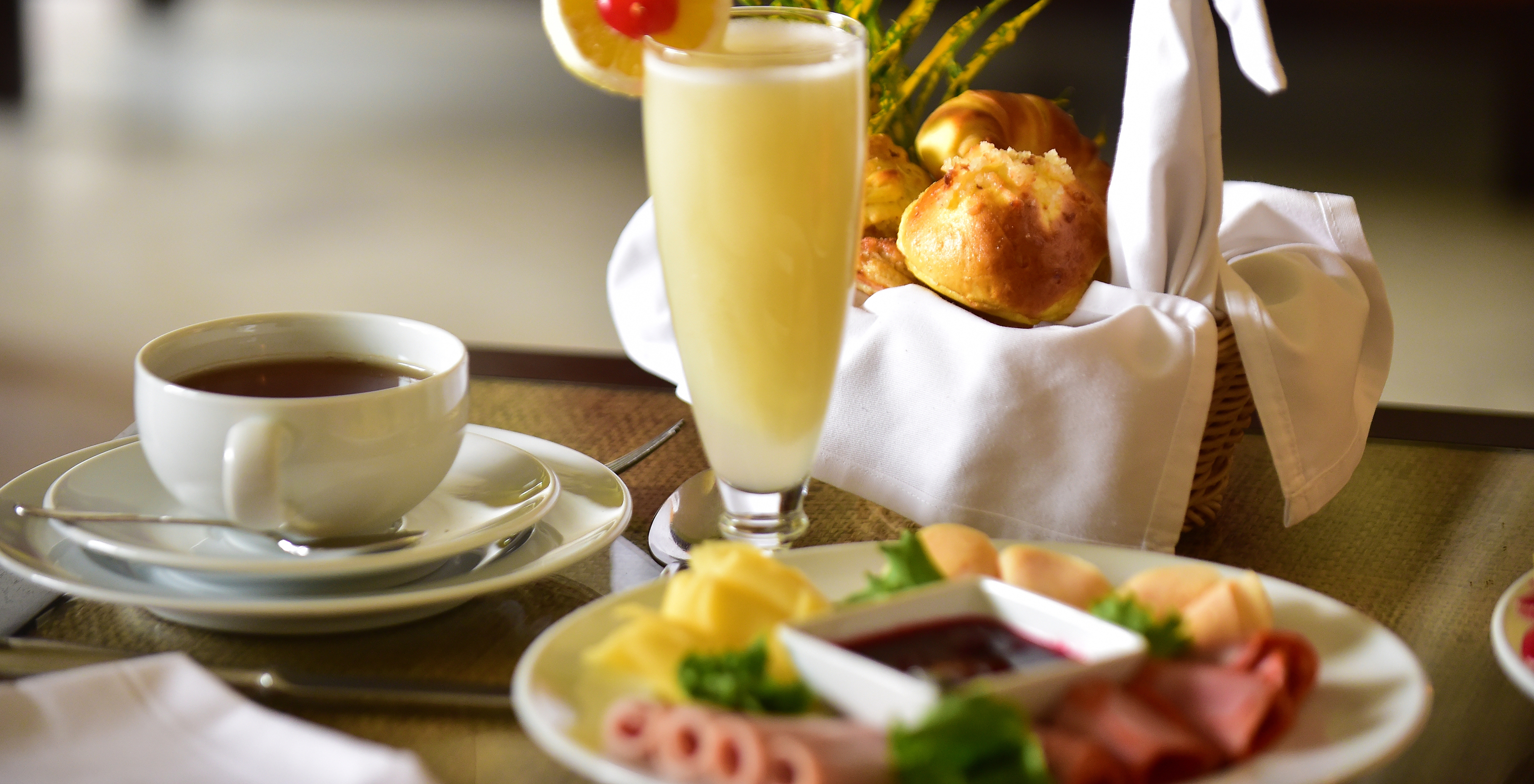 Frühstückstisch mit Kaffeetasse, einem Glas Saft und verschiedenen Brotsorten und Wurstwaren