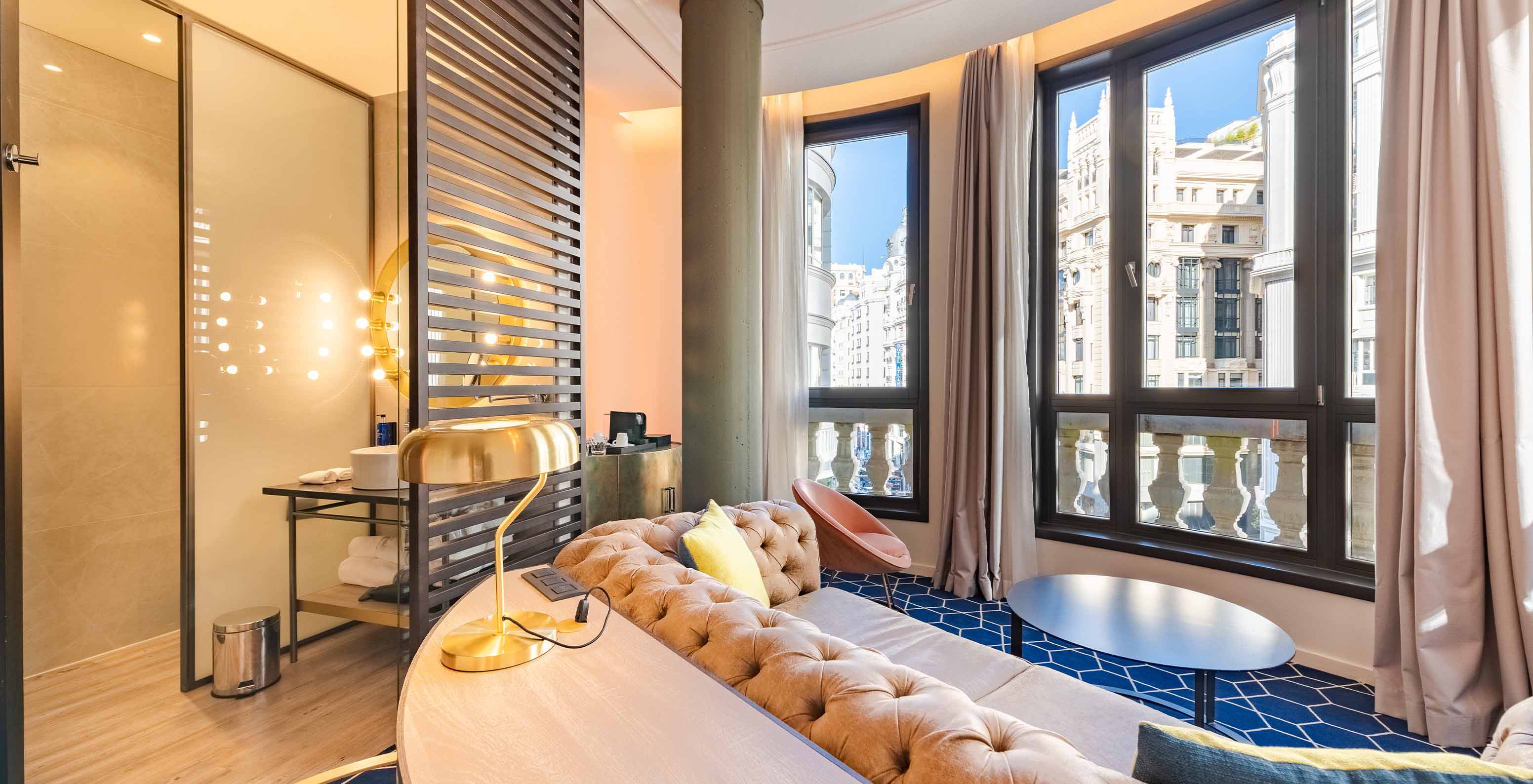 Das Fantastic 7 Zimmer im Pestana CR7 Gran Vía Madrid hat ein Sofa mit einem Tisch und große Fenster zu den Gebäuden