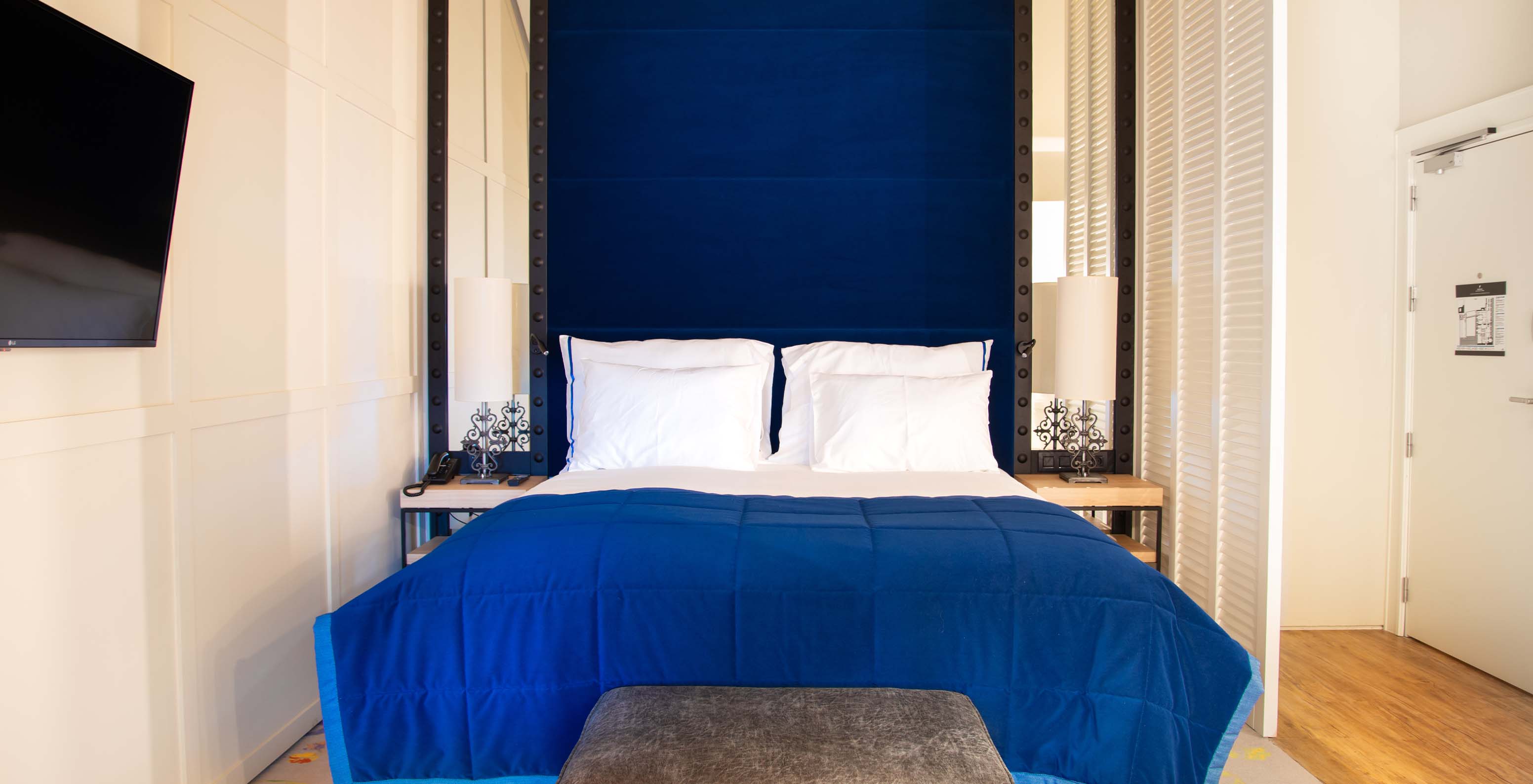 Das Loft im Pestana Plaza Mayor Madrid hat ein Doppelbett mit blauer Kopfstütze, Spiegel und Fernseher an der Wand