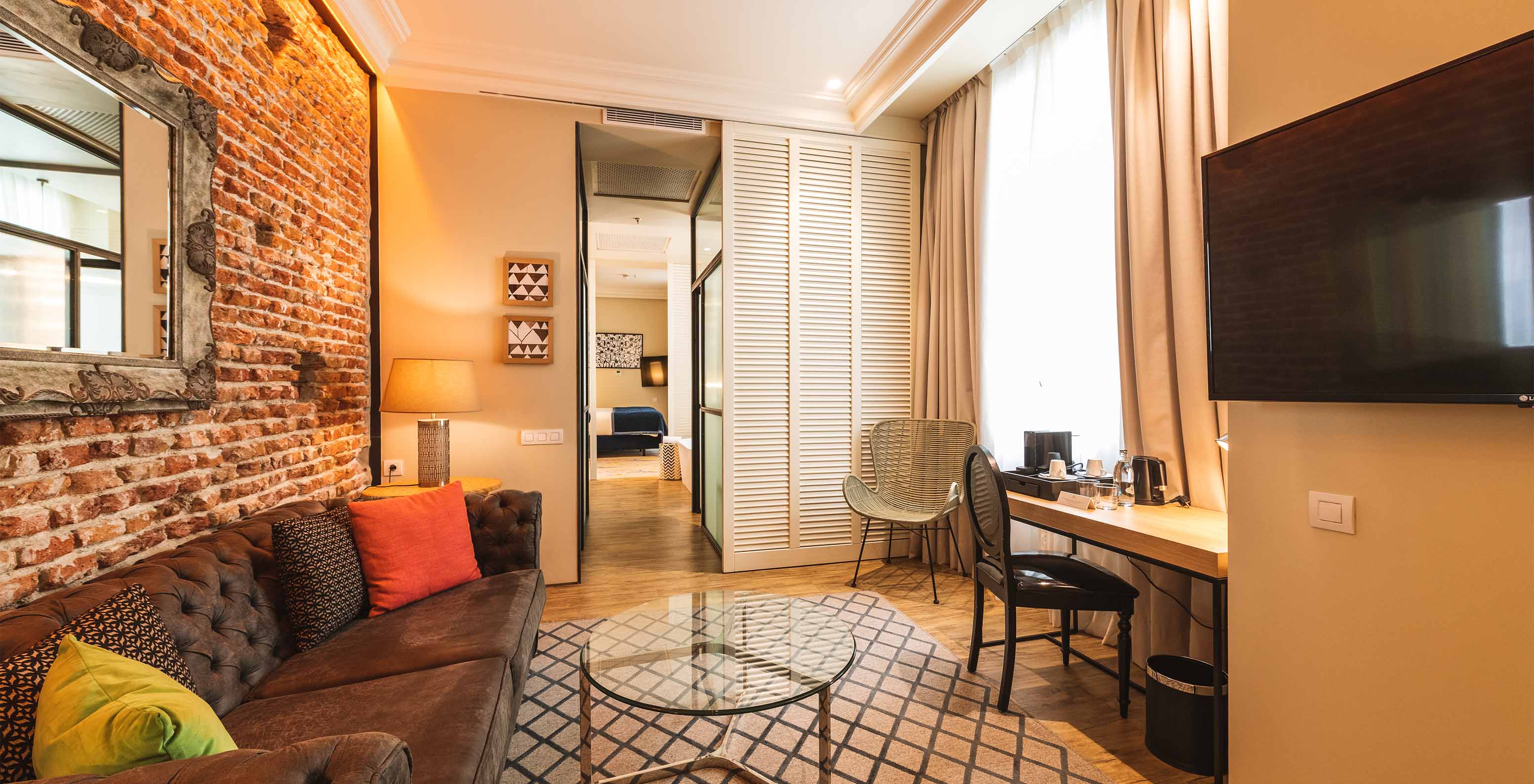 Die Suite im Pestana Plaza Mayor Madrid hat ein Wohnzimmer mit Schreibtisch, Sofa, Fernseher und Backsteinwand