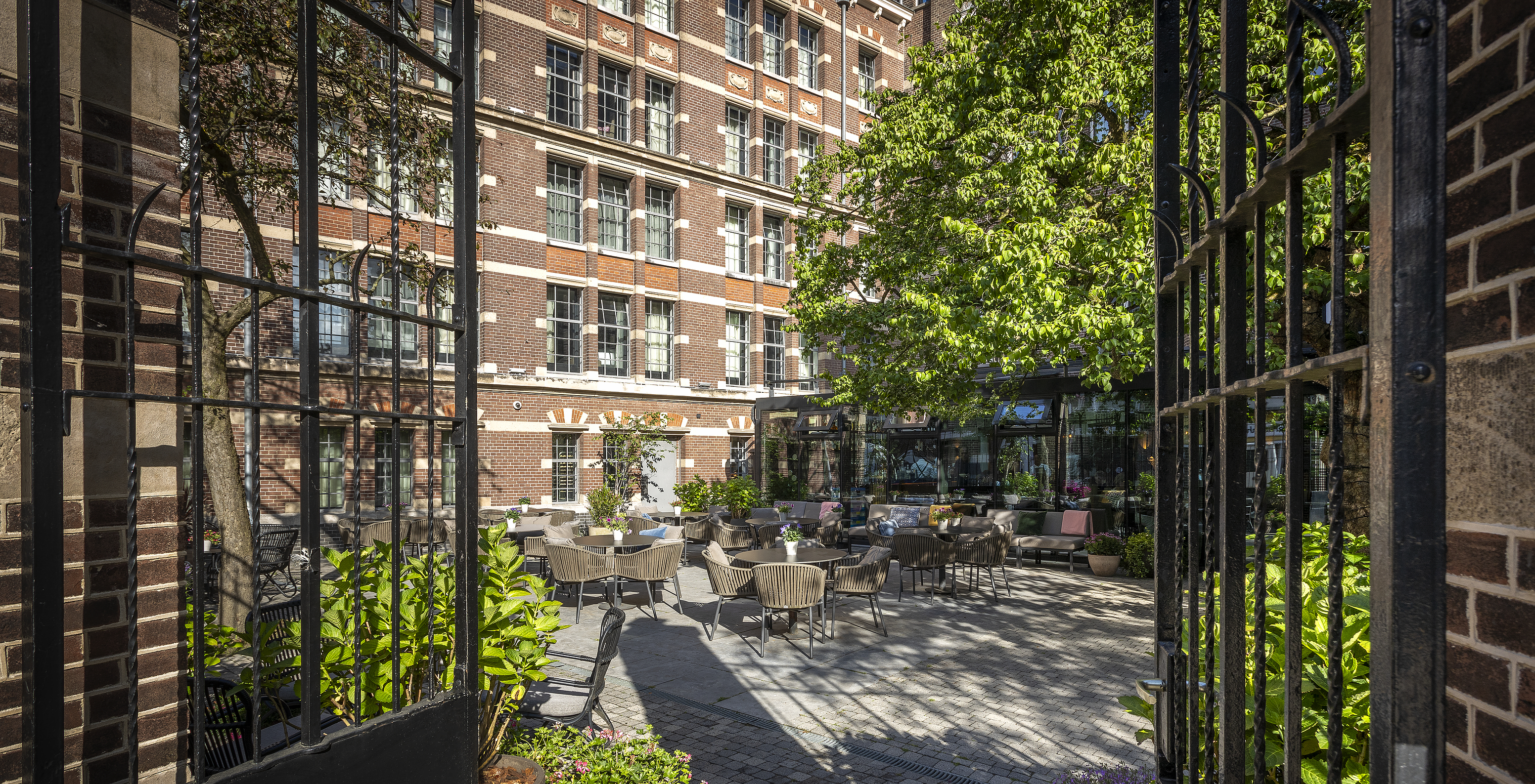 Terrasse des Pestana Amsterdam Riverside, mit runden Tischen und Stühlen, mit der Hotelfassade im Hintergrund