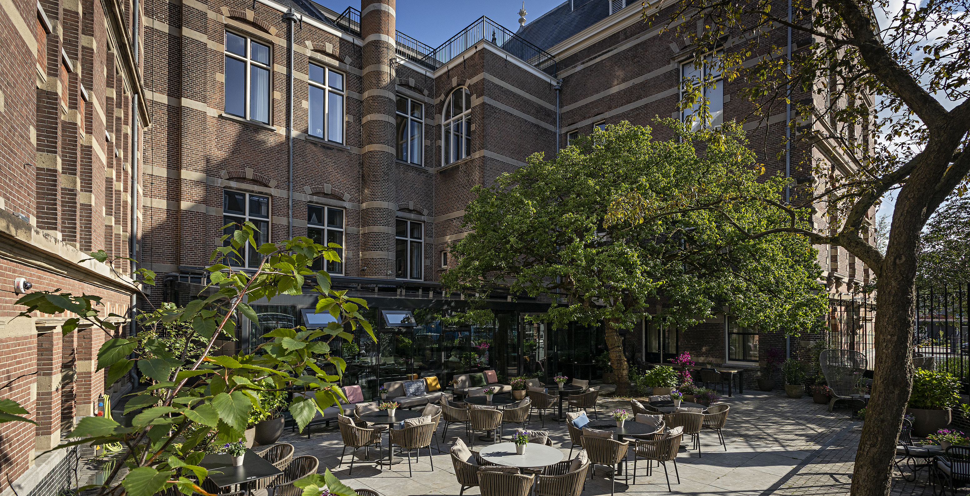 Pestana Amsterdam Riverside Hotel im Zentrum von Amsterdam hat eine Terrasse mit mehreren Tischen und Stühlen und Bäumen