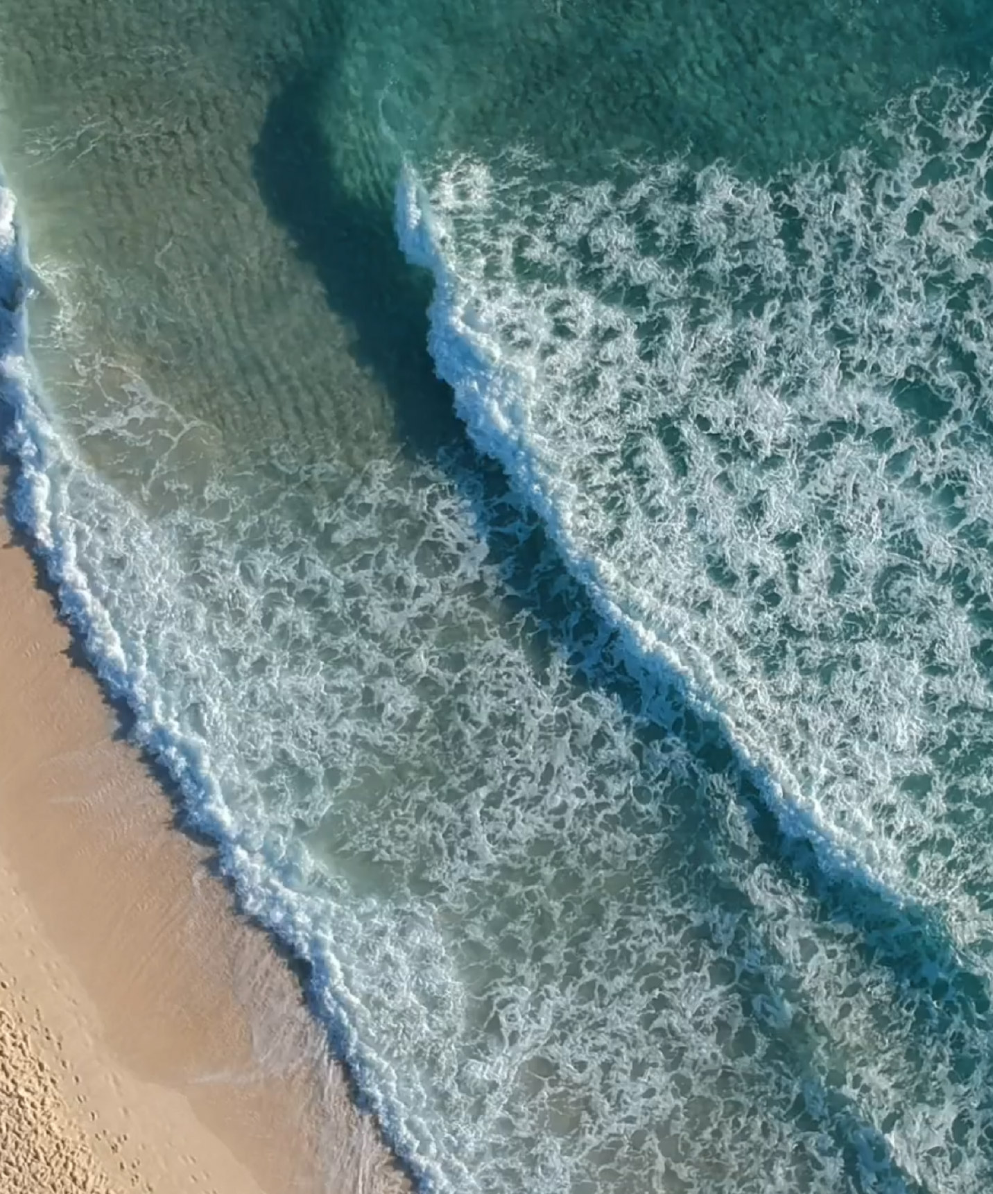 Luftaufnahme eines Strandes mit Wellen, die am goldenen Sand brechen, in einem Hotel der Pestana Hotels & Resorts