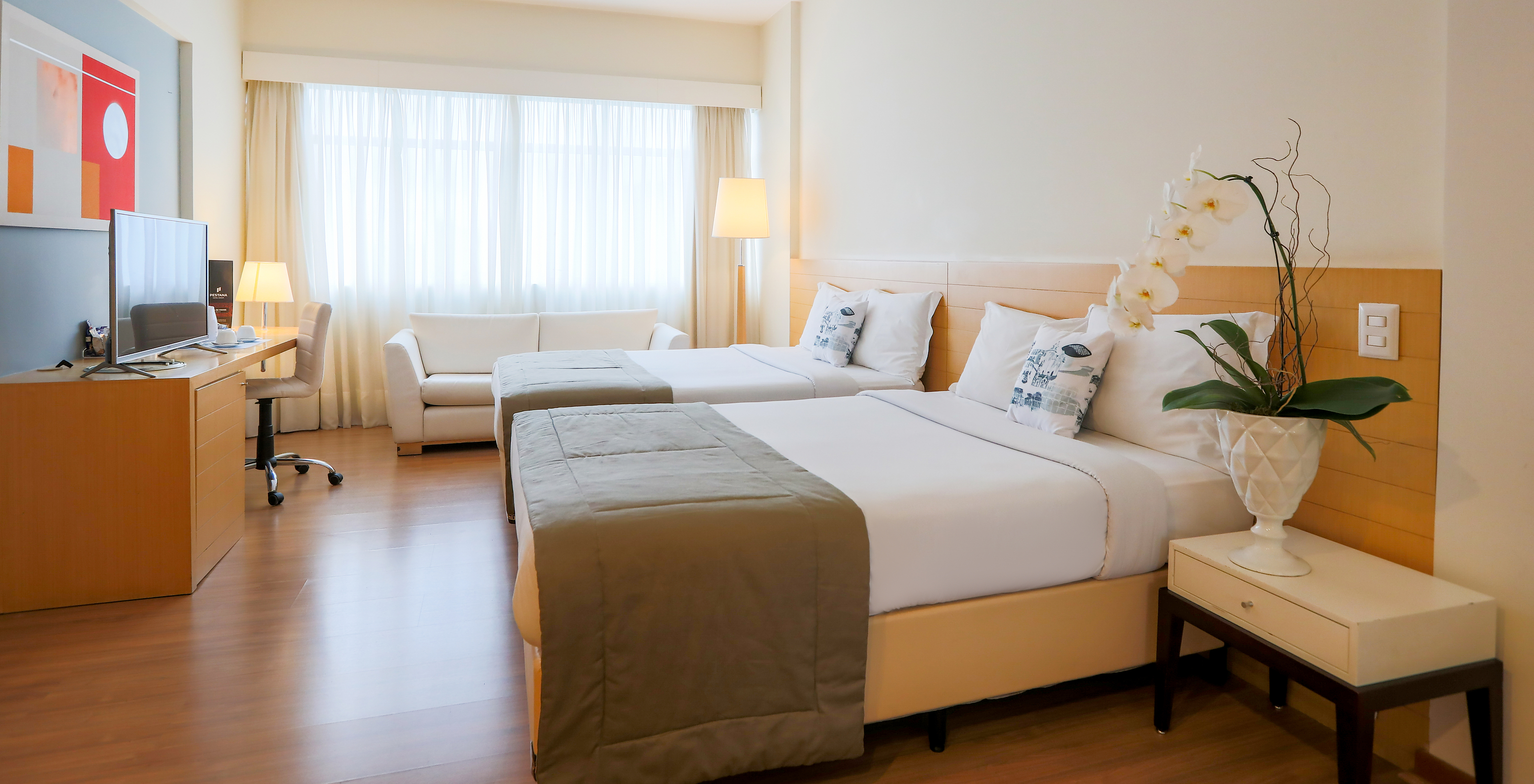 The Family Room at Pestana Curitiba has two double beds, a desk with a television, and a double sofa by the window