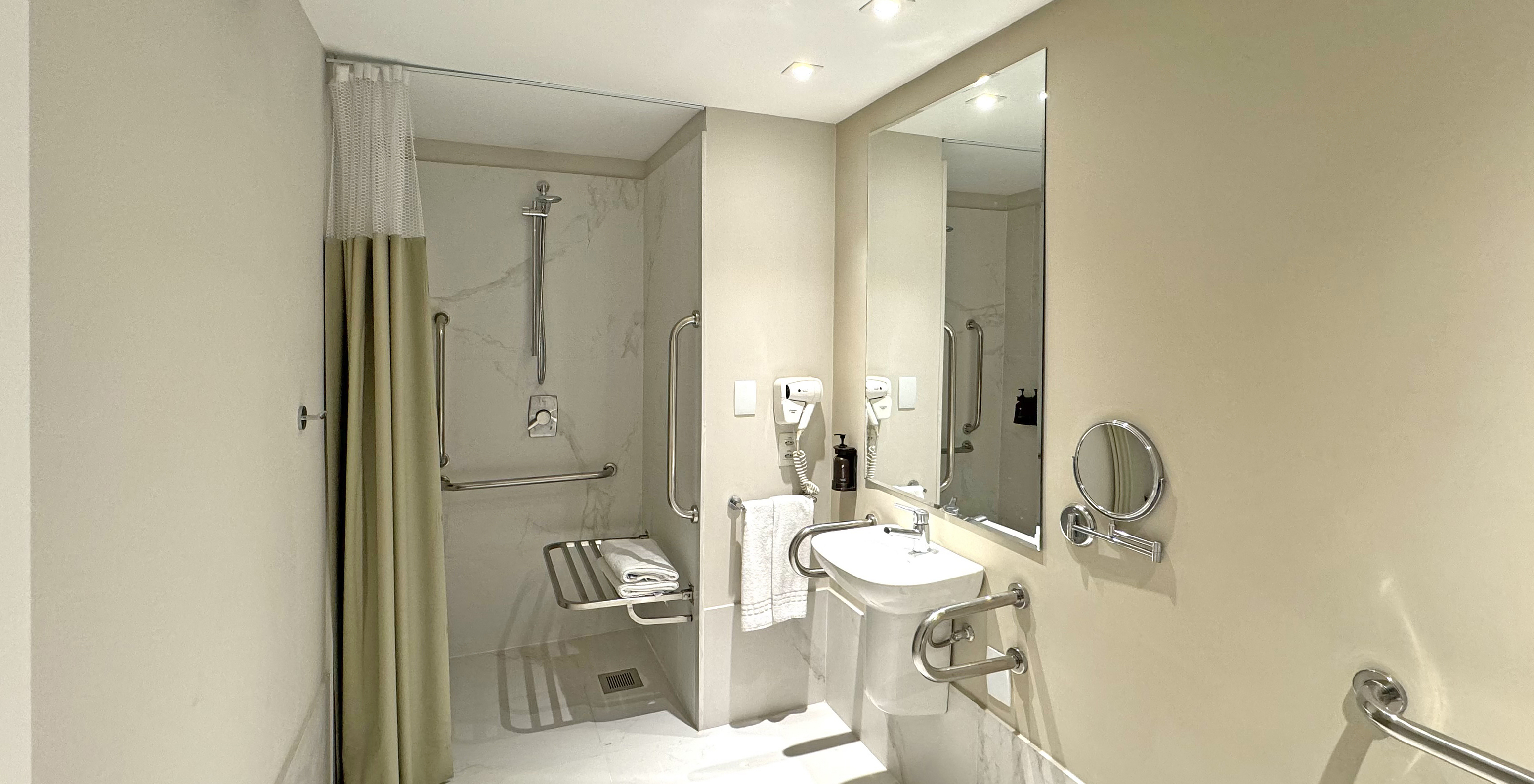 The Adapted Room of Pestana Rio Atlântica has an adapted bathroom with shower, sink, mirror, and hairdryer