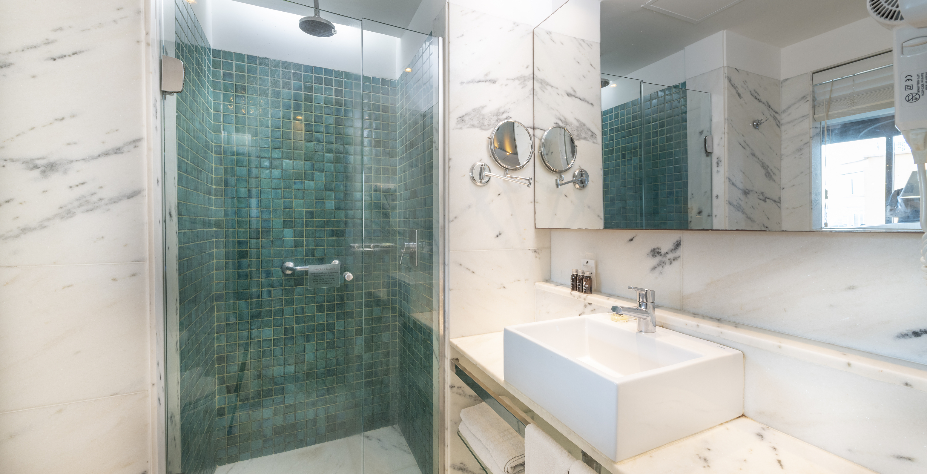 The Lateral Sea View Room of Pestana Rio Atlântica has a bathroom with shower, sink with mirror, and magnifying mirror