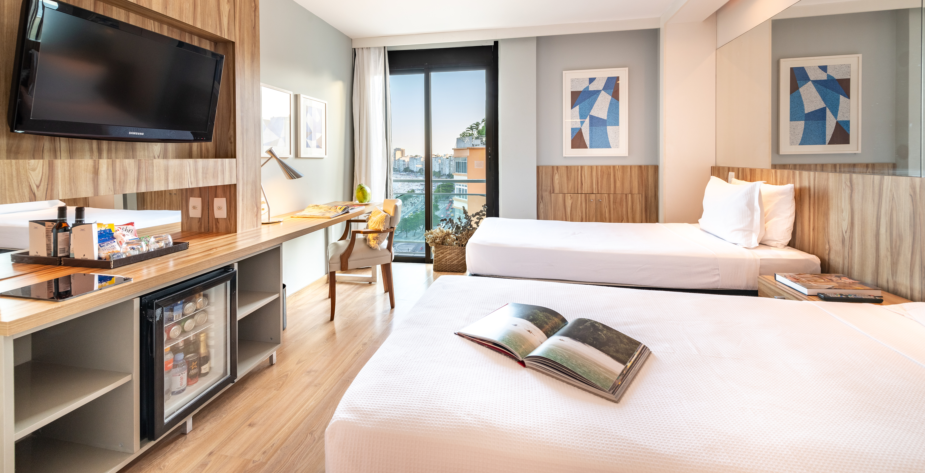 The Lateral Sea View Room of Pestana Rio Atlântica has two beds, a television, and a window with a view of Copacabana Beach