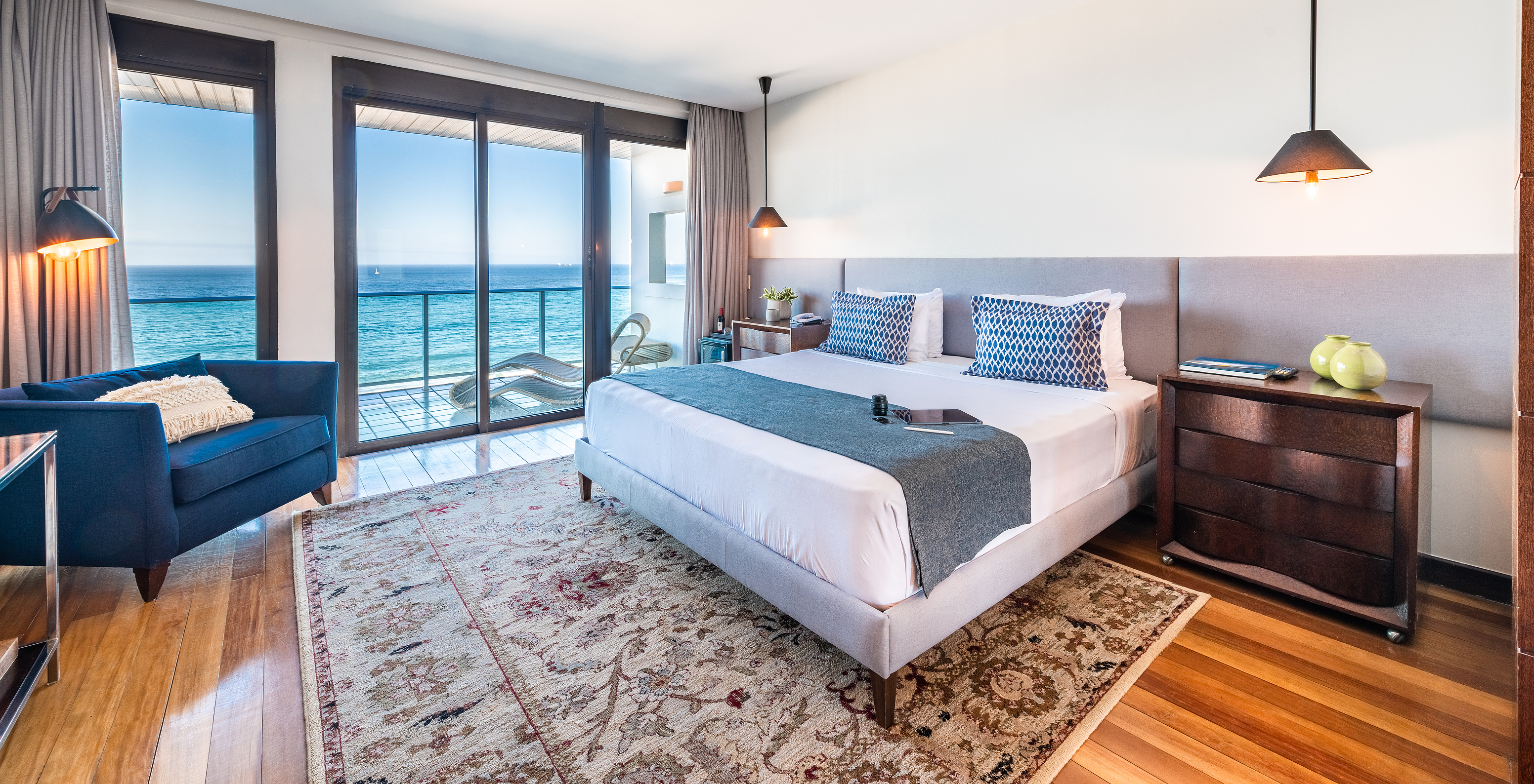 The Presidential Suite of Pestana Rio Atlântica has modern decor, a double bed, armchair, and balcony with sea view