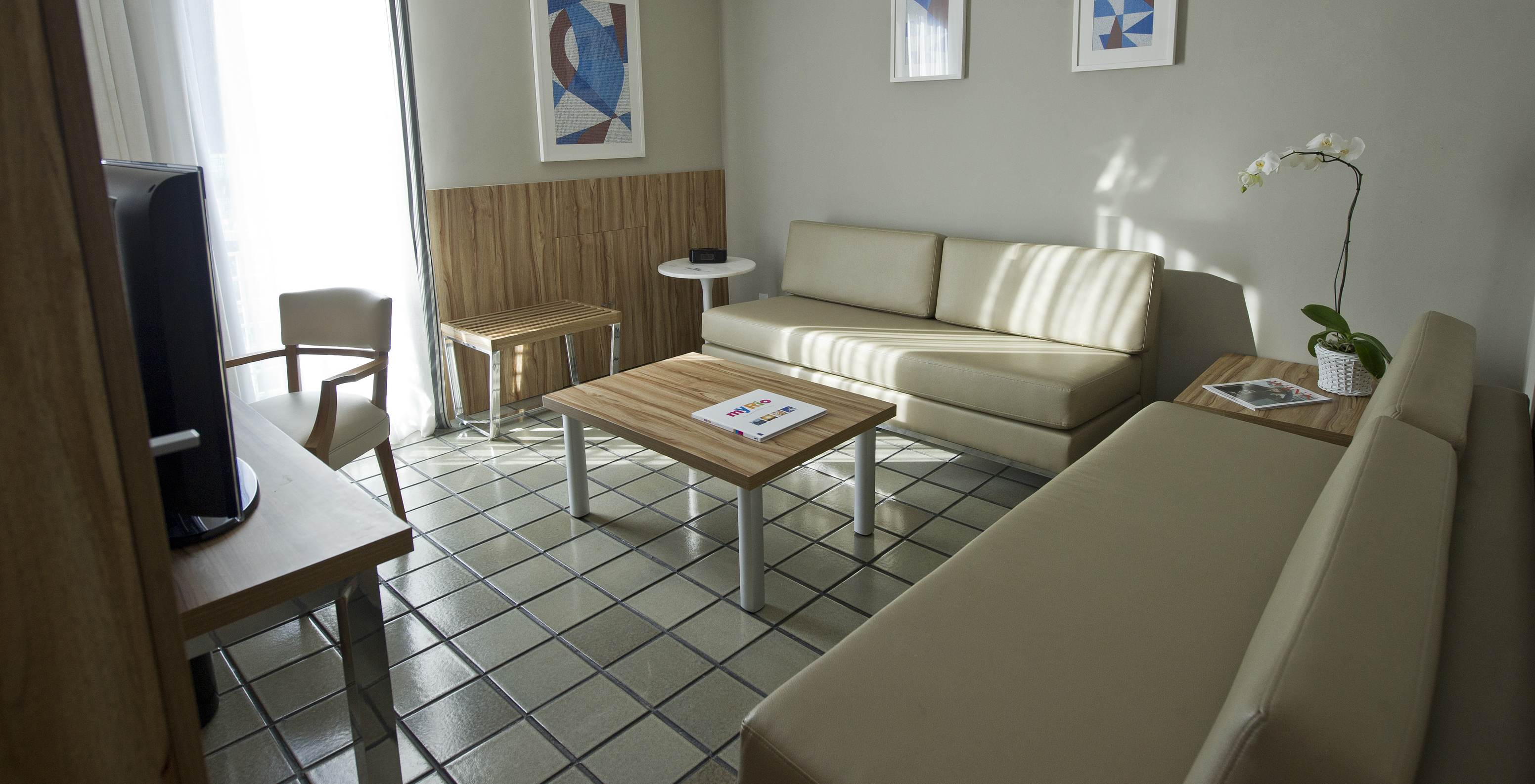 The Suite of Pestana Rio Atlântica has a living room with two comfortable beige sofas, a side table, and a television