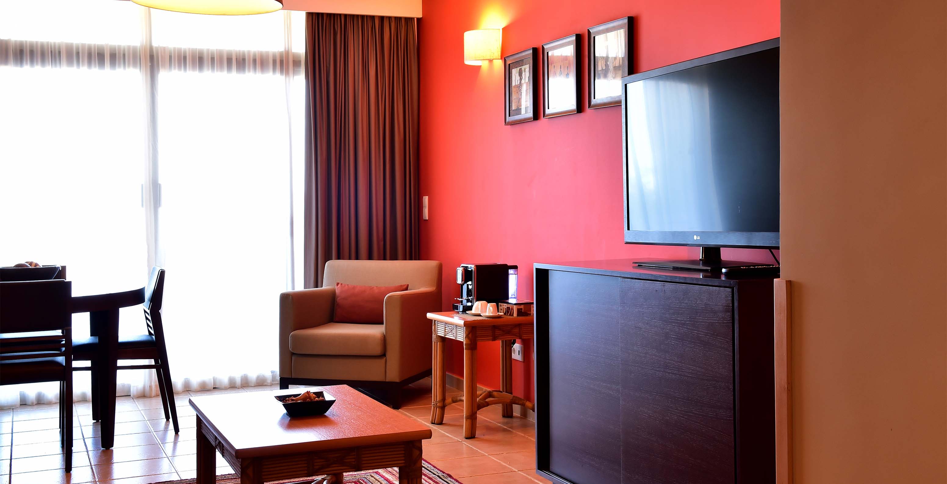 The Suite at Pestana Tropico features a living room with dining table, armchair, coffee table, and a television