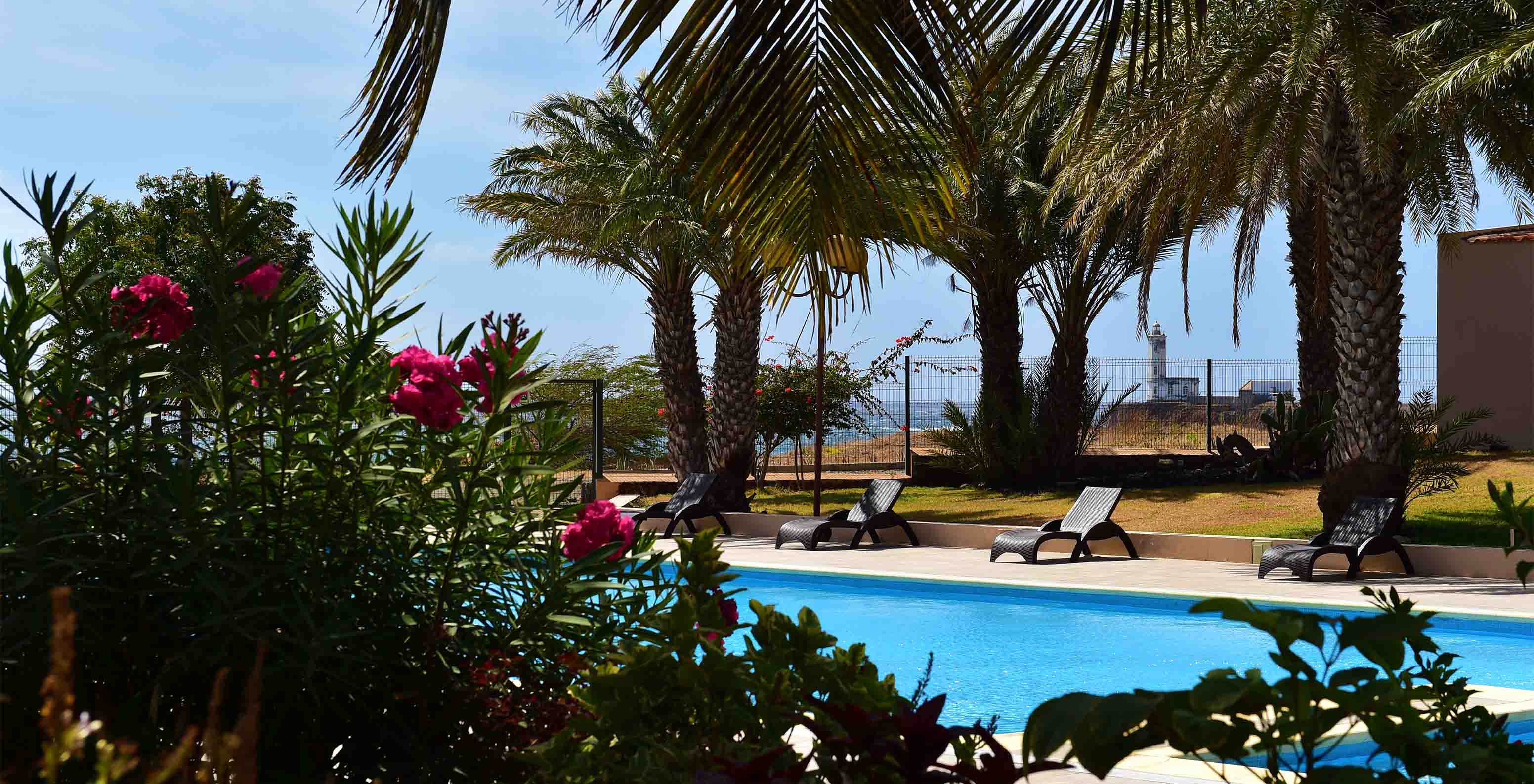 Outdoor space of Pestana Tropico with pool, sun loungers, palm trees, and the sea in the background