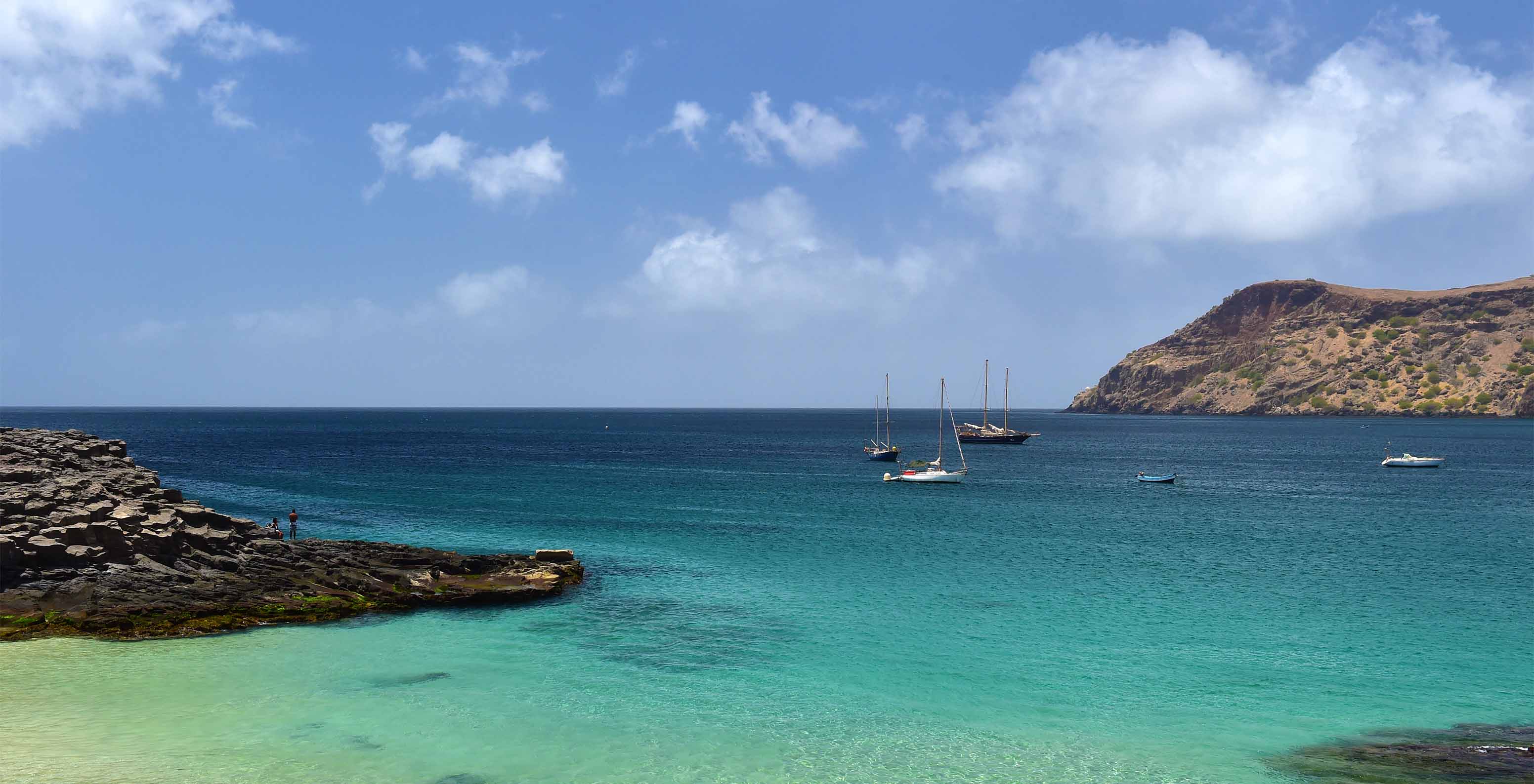 View of the ocean with crystal-clear water and a few boats docked in the background