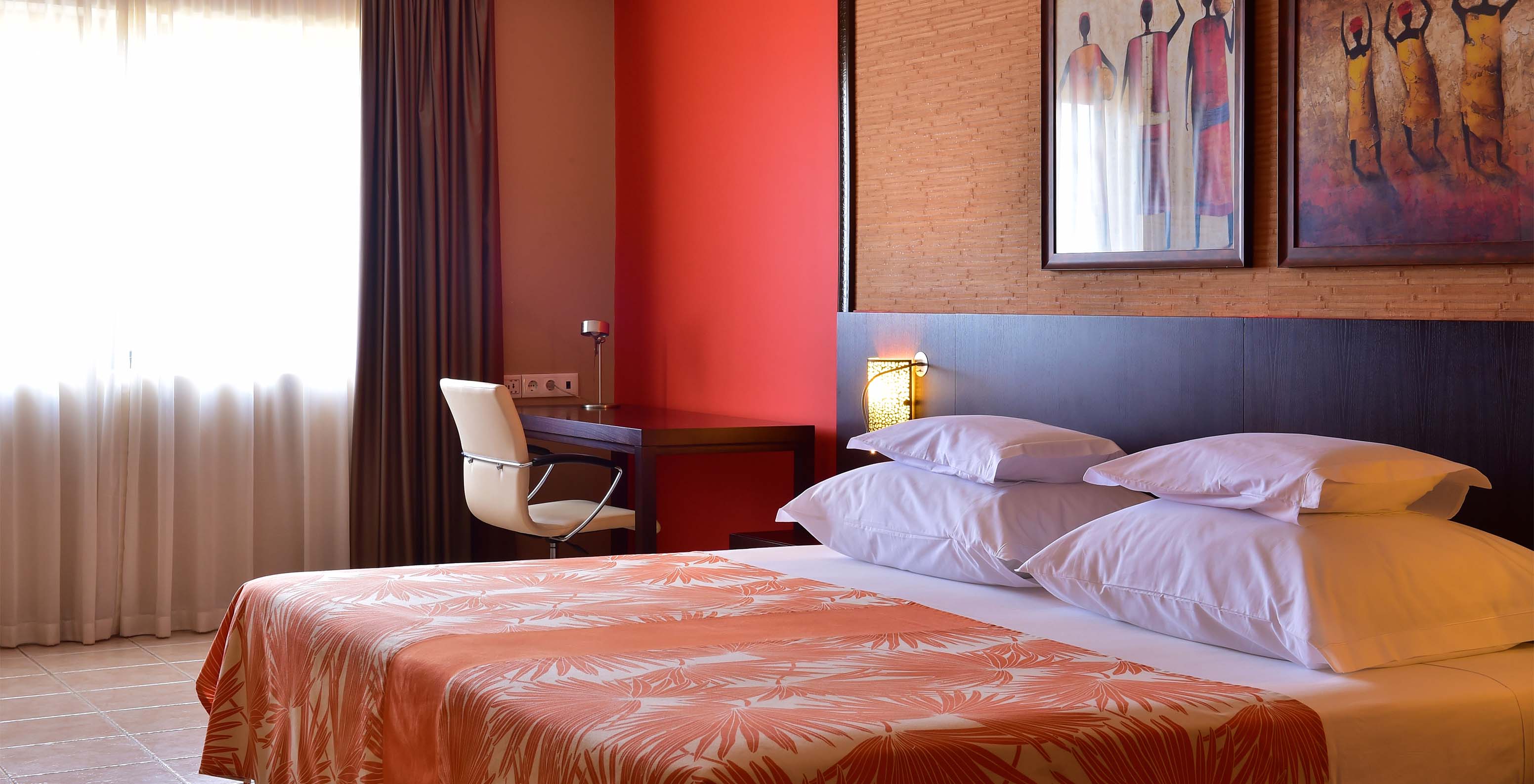 The Standard room at Pestana Tropico features a double bed, desk with chair, and bedside table with lamp