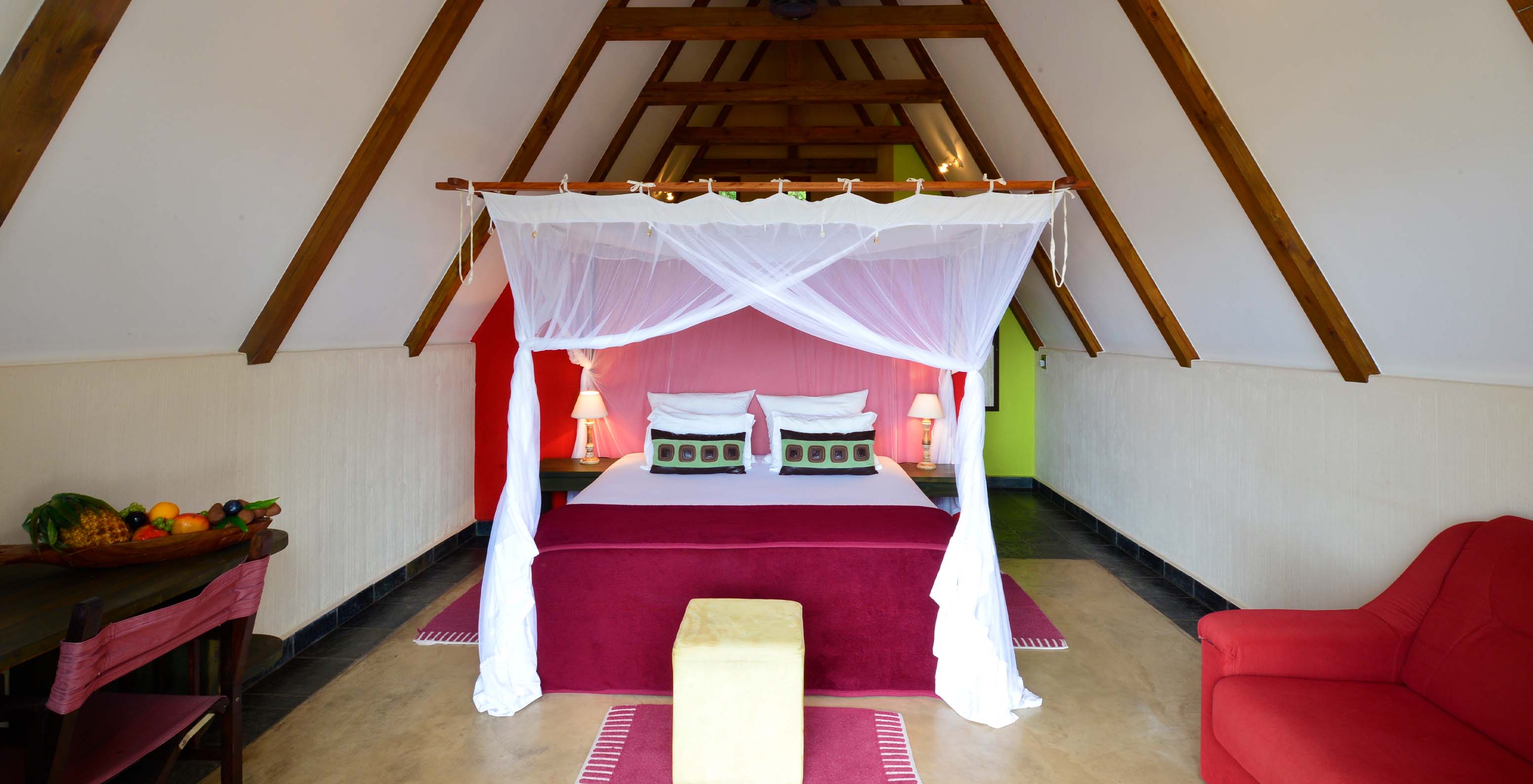 Bungalow T1 at Pestana Bazaruto Lodge has a double bed with canopy, a sofa and a desk with a bowl of fruit