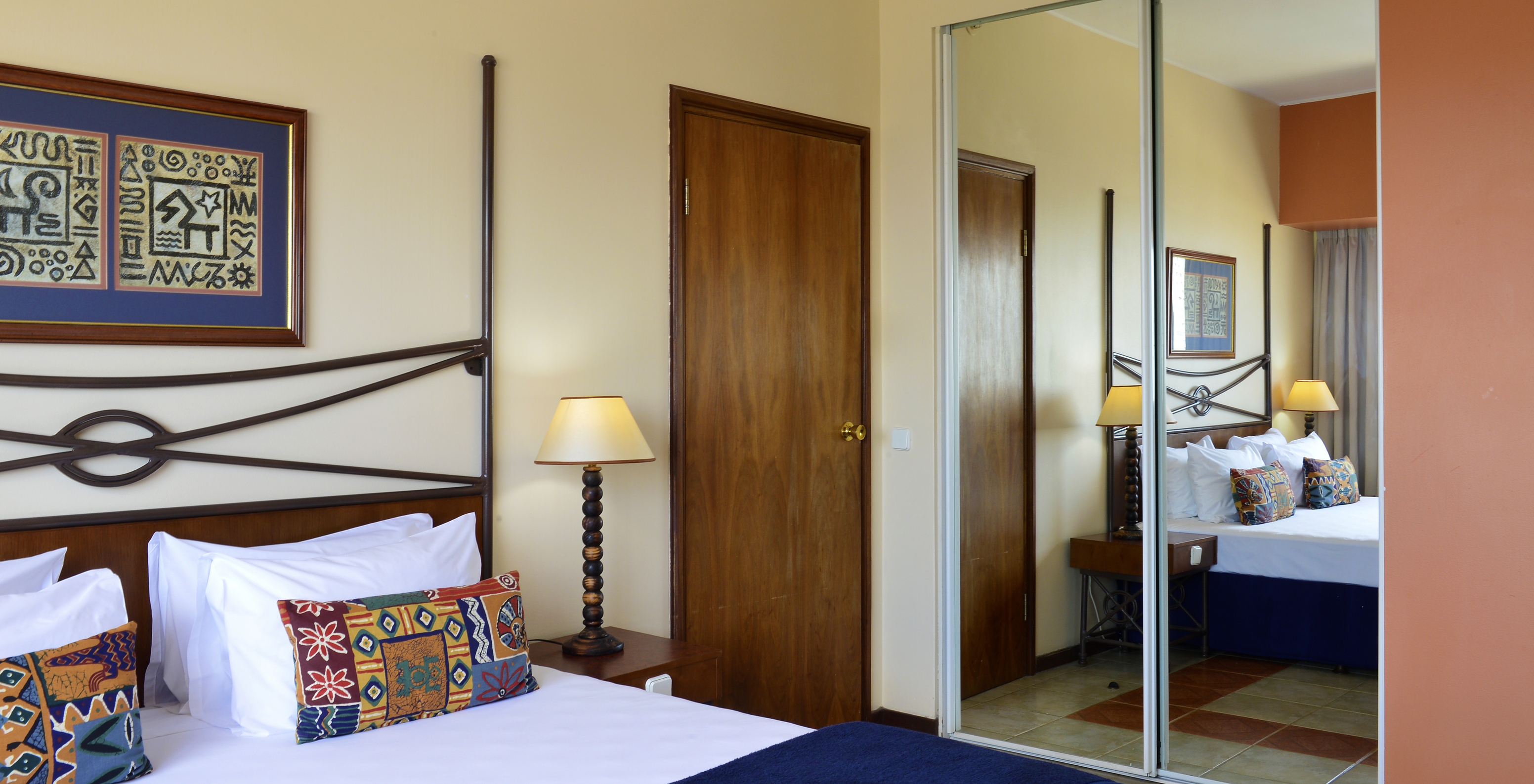 The Standard Double of Pestana Rovuma has a double bed, an African-themed painting, and a wardrobe with a large mirror