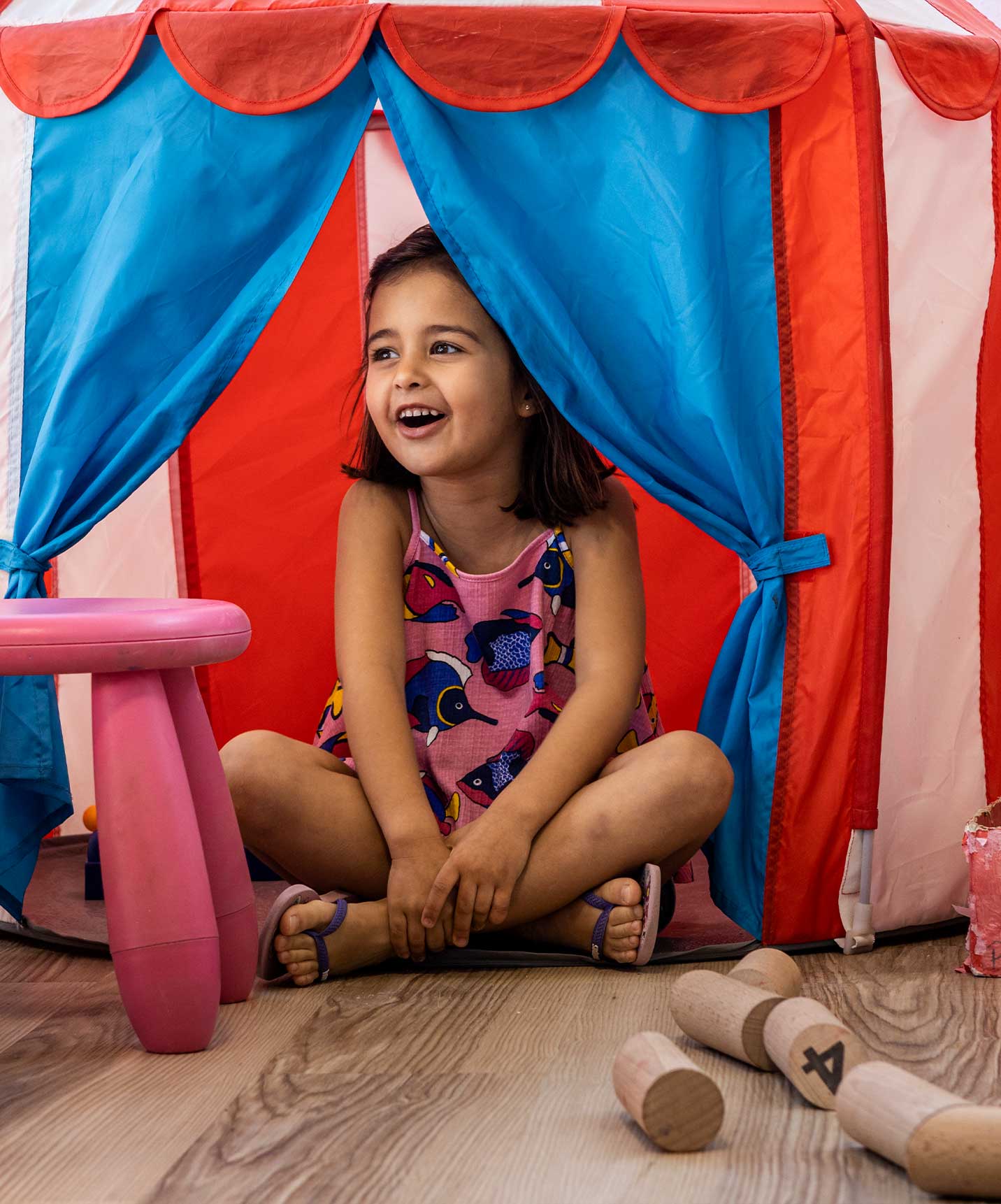 A child happily playing at the Kids Club, hiding in a red and blue tent