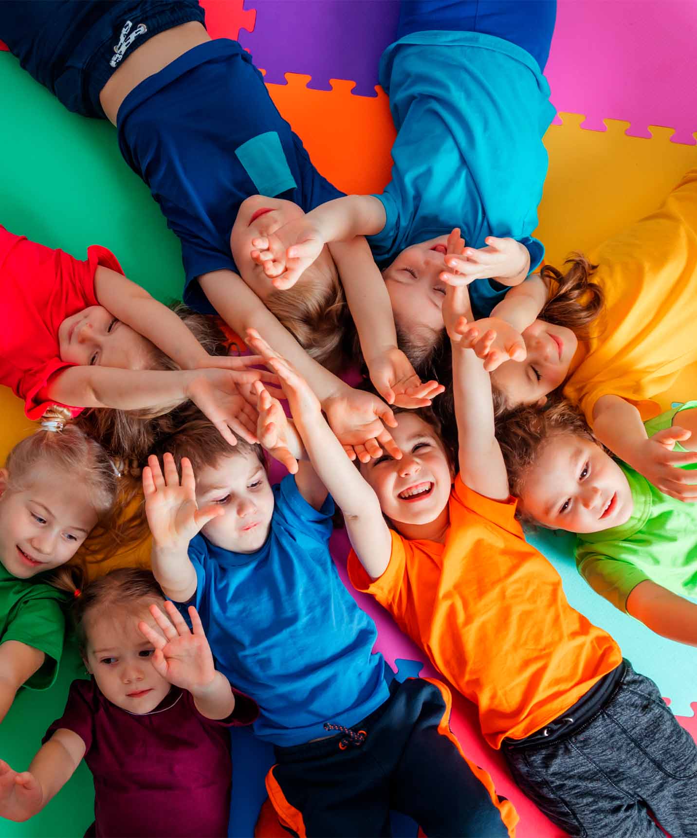 Group of smiling children in blue, orange, green, red, and purple t-shirts on colorful square floor