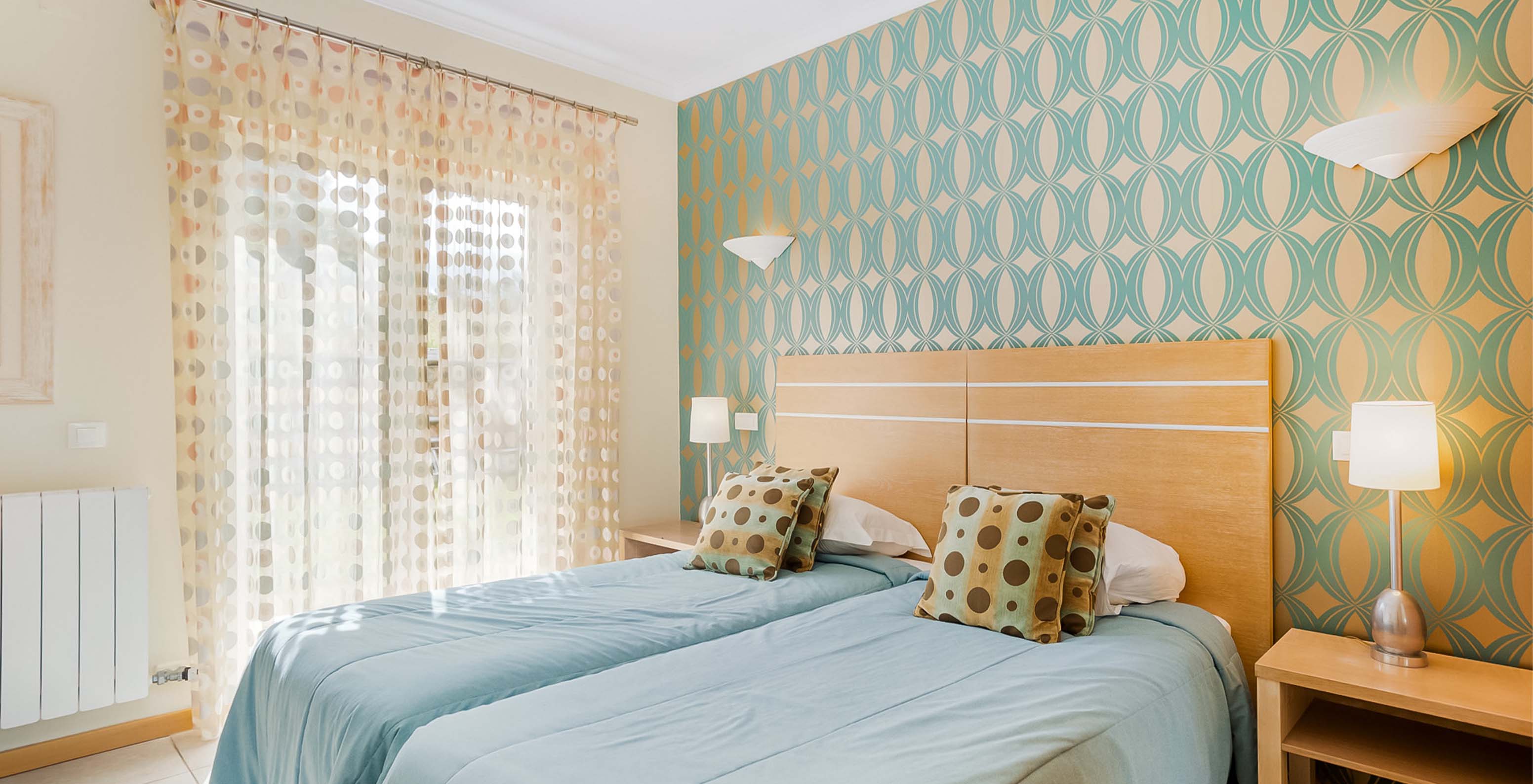 The T1 Apartment at Pestana Carvoeiro Golf has a bedroom with two single beds, wallpaper, and colorful curtains