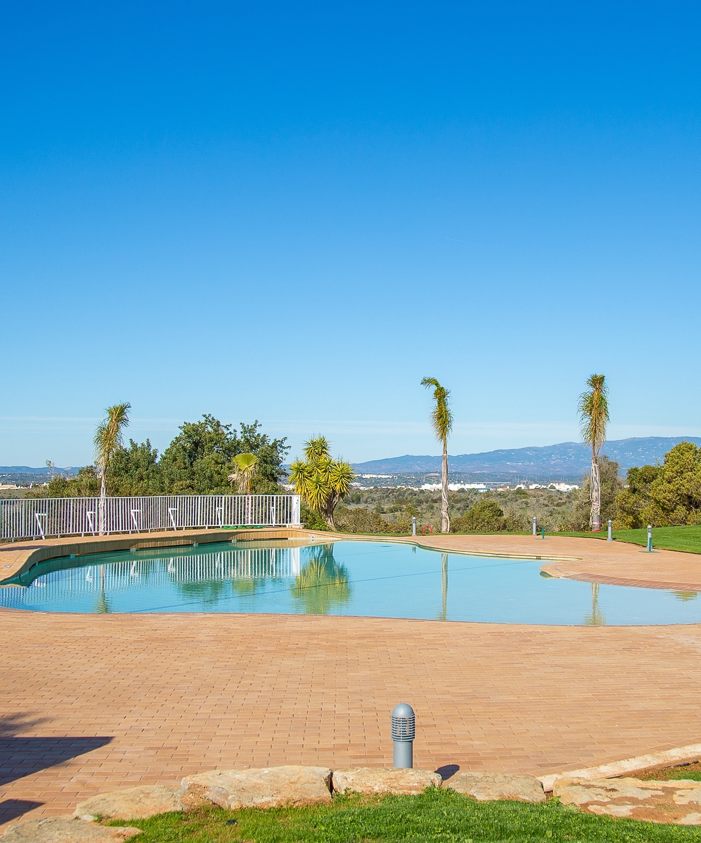 Outdoor pool on a sunny day at Pestana Gramacho Residences, with a panoramic view of the city in the background